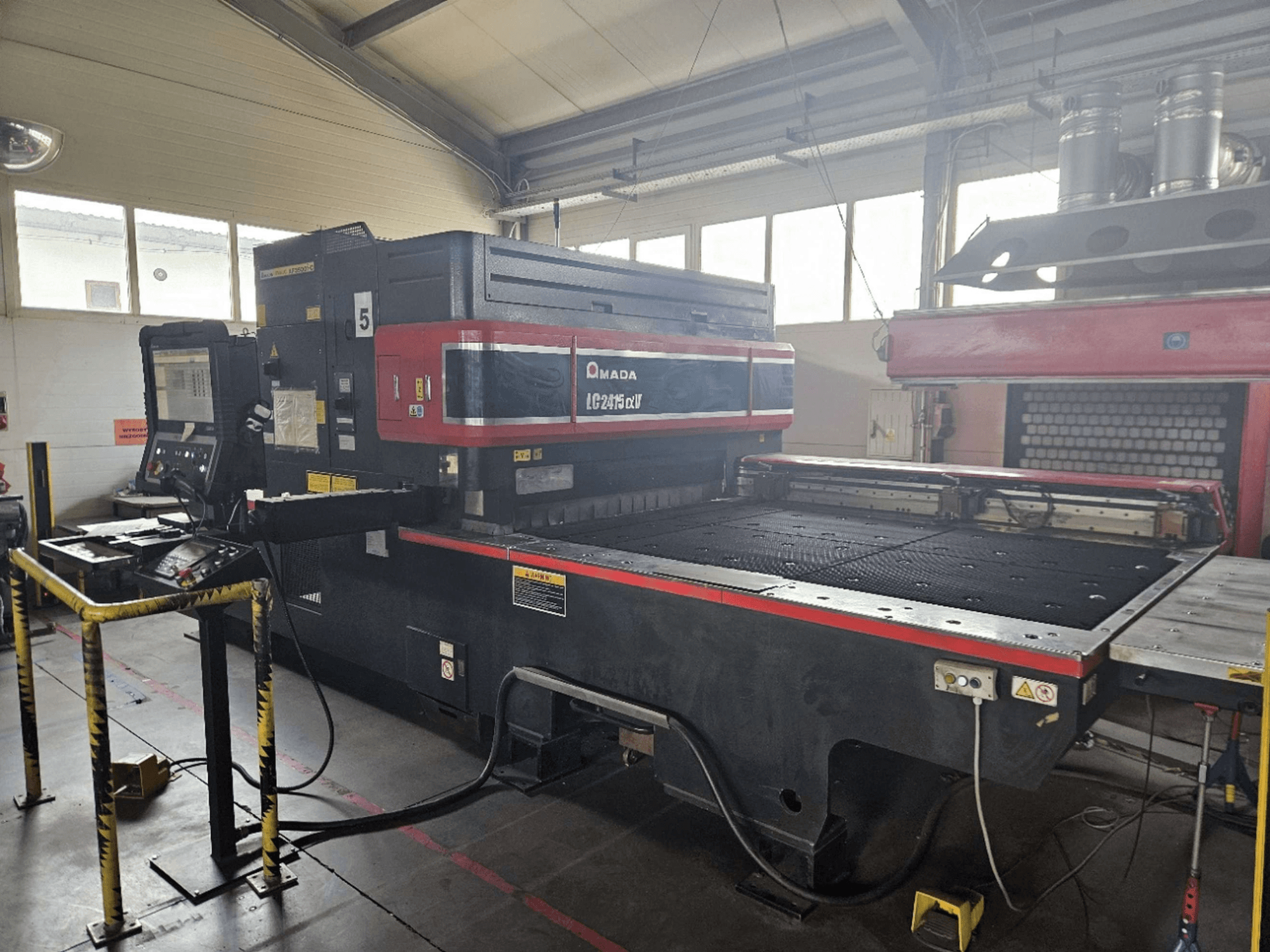 AMADA LC2415 Alpha 5 CO₂ lézervágó gép, elölnézet, amelyen látható a vezérlőpanel és a vágóasztal a biztonsági korlátokkal.