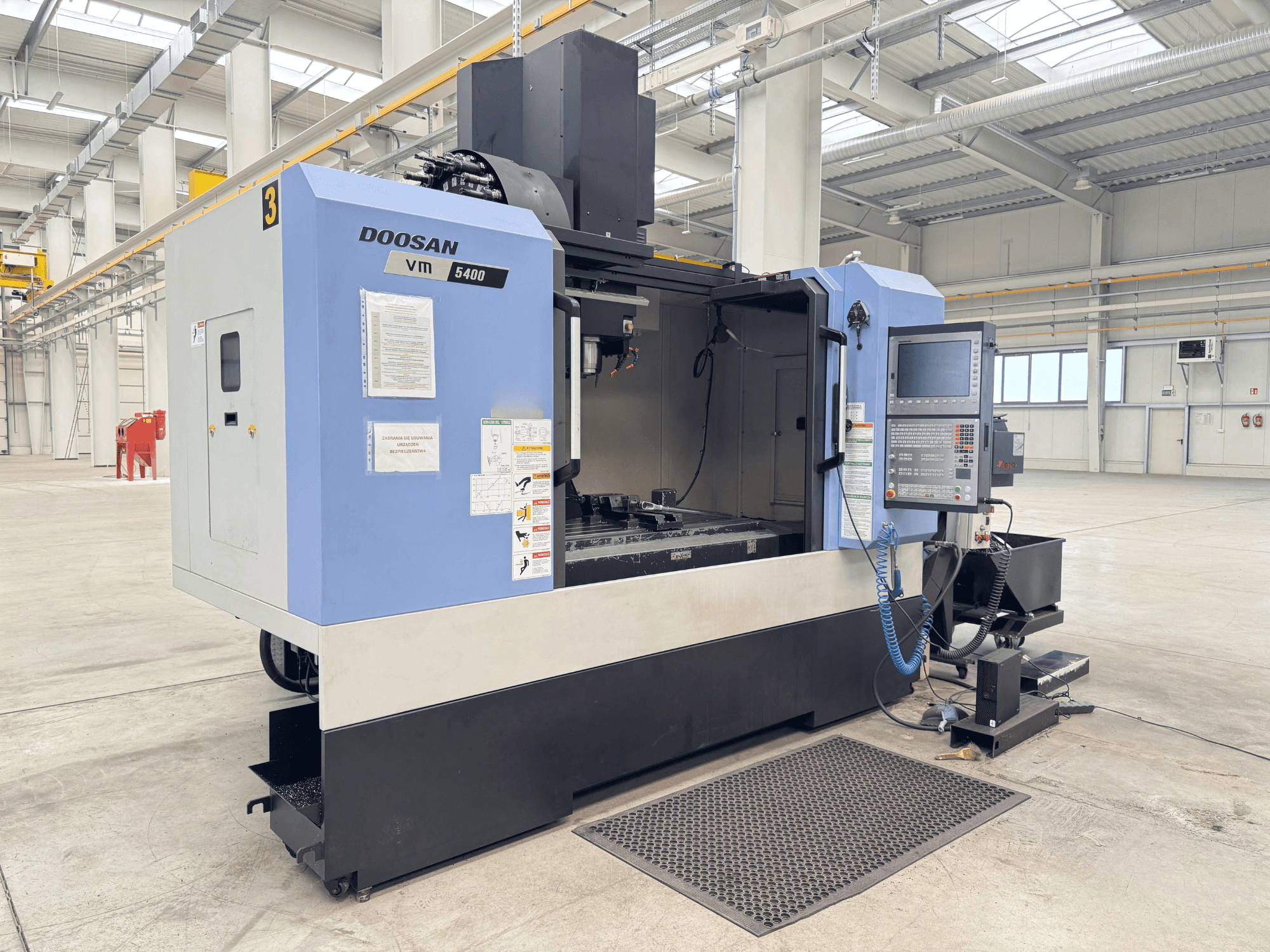 DOOSAN VM 5400 függőleges megmunkálóközpont, elölnézetben a vezérlőpanel és a munkaterület tágas ipari környezetben.