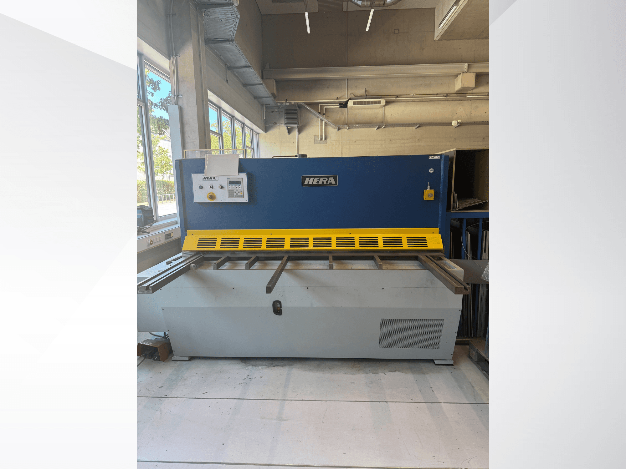 A HERA TS 2000x6 hidraulikus vágógép elölnézetben, kék-sárga színkombinációval, vezérlőpanellel és vágóasztallal.