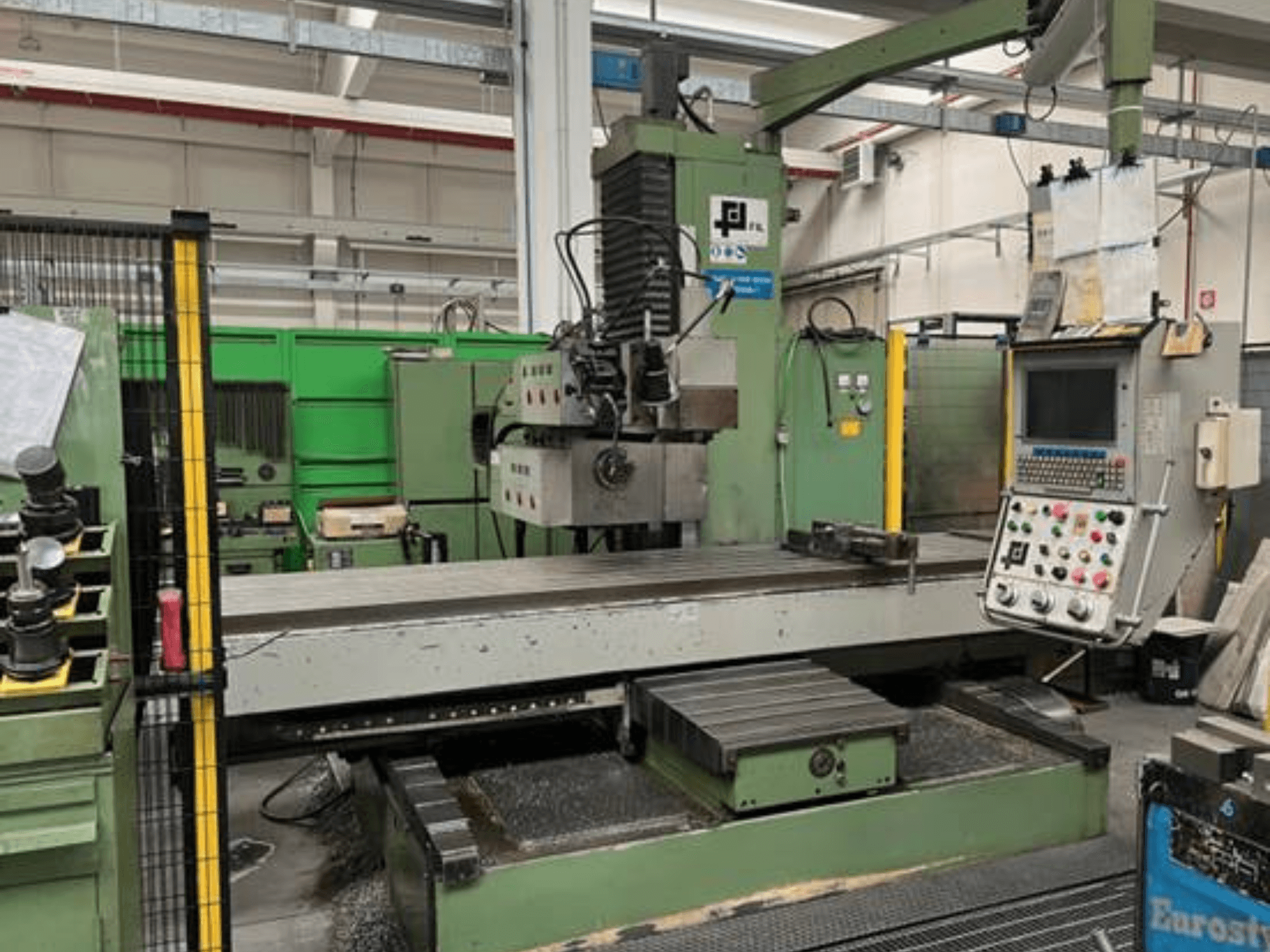 Ipari marógép a JFL-től, elölnézet a vezérlőpanellel, nagy lapos asztallal és fémforgáccsal a padlón.