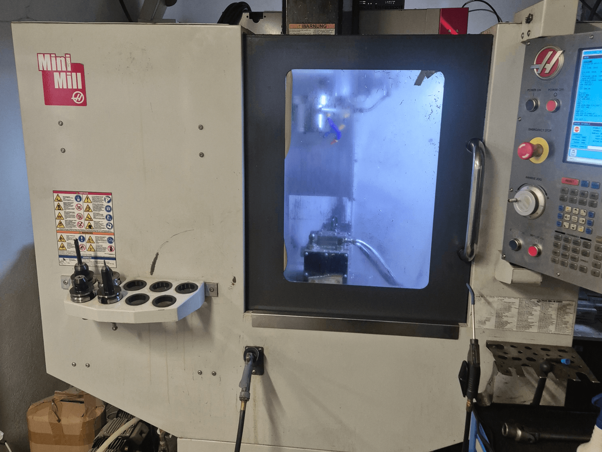 A HAAS Mini Mill elülső nézete, a vezérlőpanel, a szerszámtartók és a hűtőközeggel ellátott megmunkálási területre nyíló kilátás.