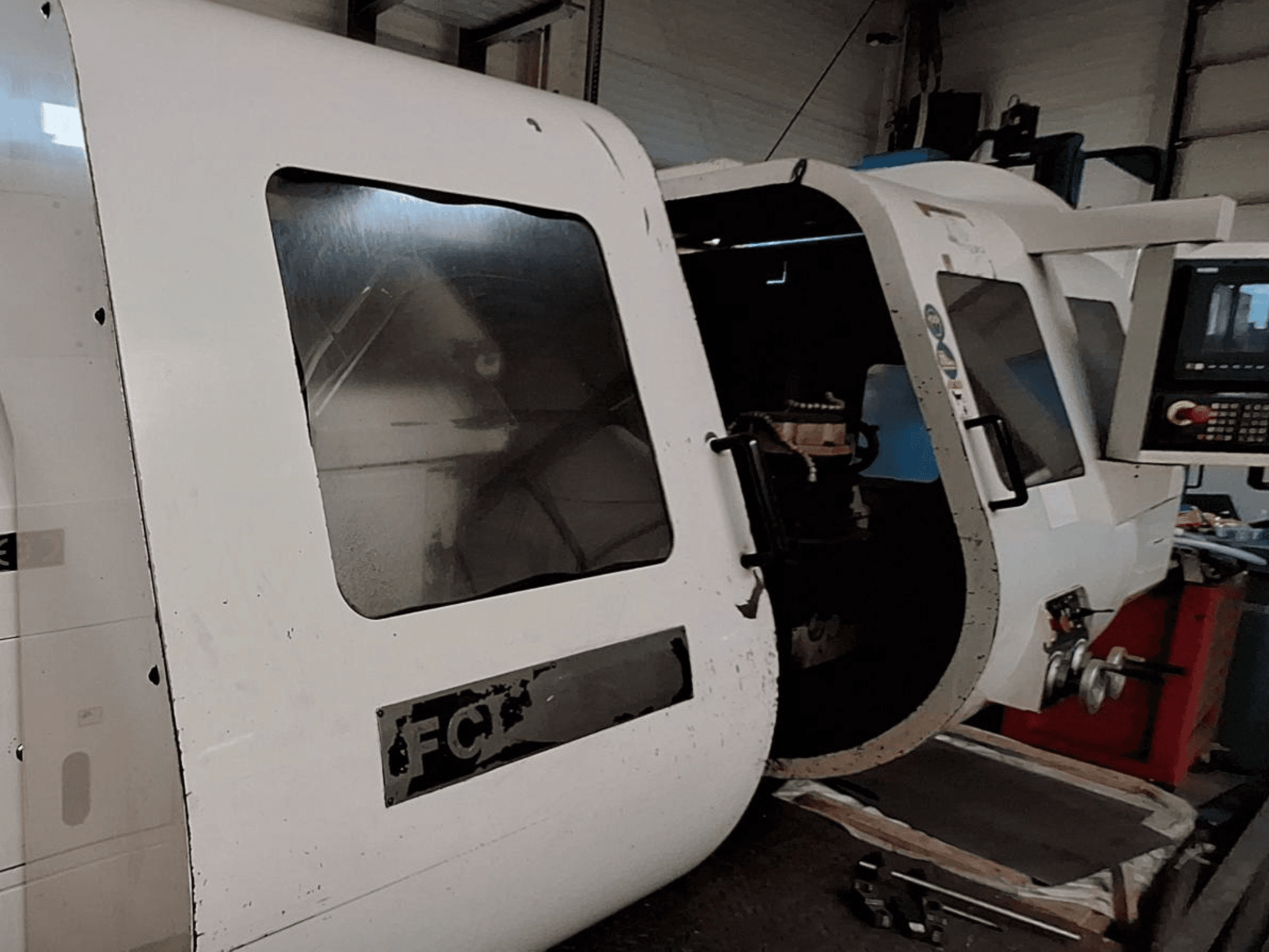 Fehér CNC-gép látható vezérlőpanellel és nyitott ajtóval, a belső alkatrészek bemutatásával; elölnézet. Márka: A gépet a márkaképviselők és a gyártó cégek által gyártott gép: FCT.