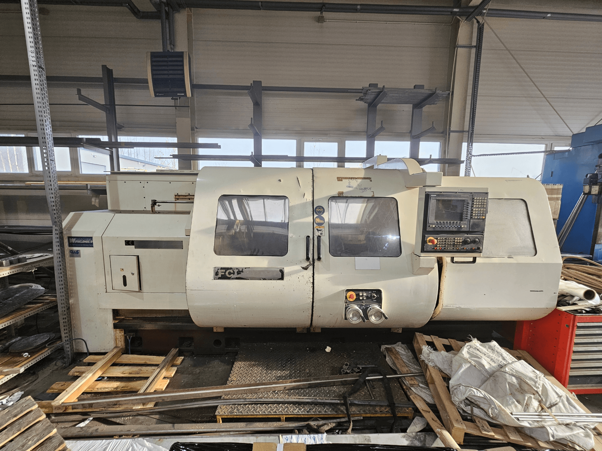 Wabeco CNC eszterga, oldalnézet, vezérlőpanel, ablakok és munkaterület; a gépek fából készült raklapokon, műhelyben.