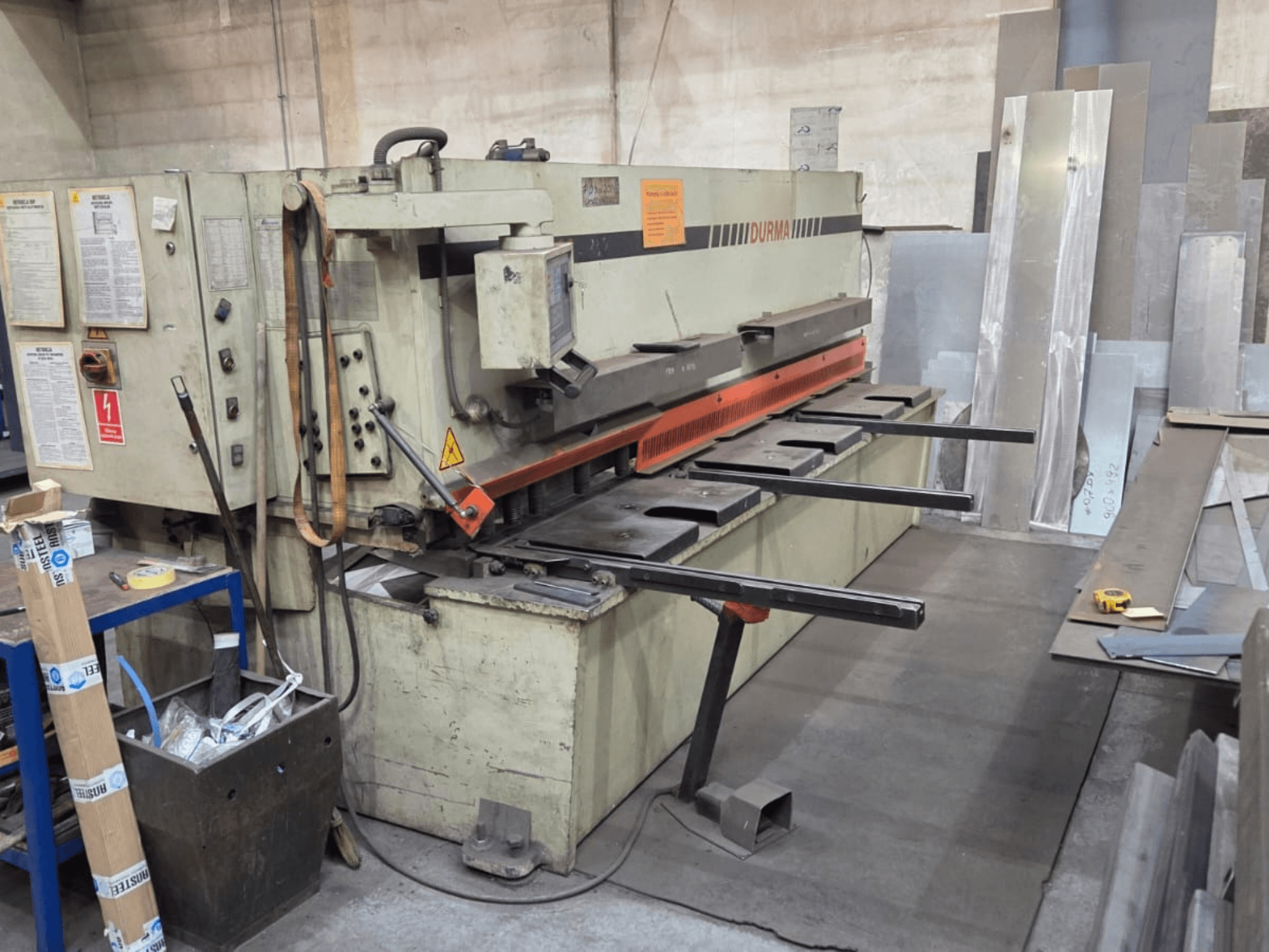 Durma SB 3060 hidraulikus nyírógép, elölnézet, a kezelőszervek, a vágópenge és a fémlemezek a munkaterületen.