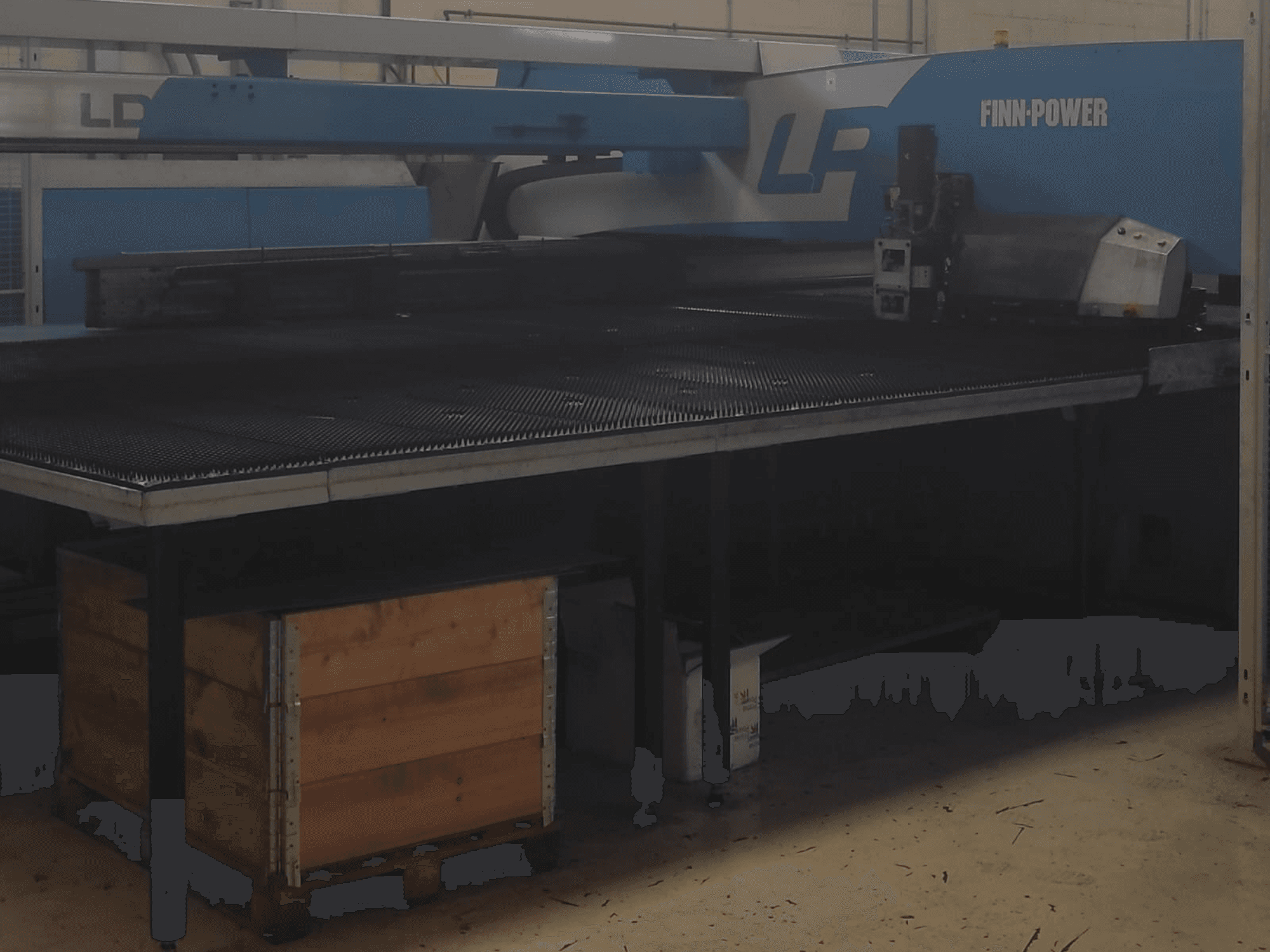 Finn-Power LP vágógép egy gyárban, elölnézetben, alatta texturált fémasztal és faláda.