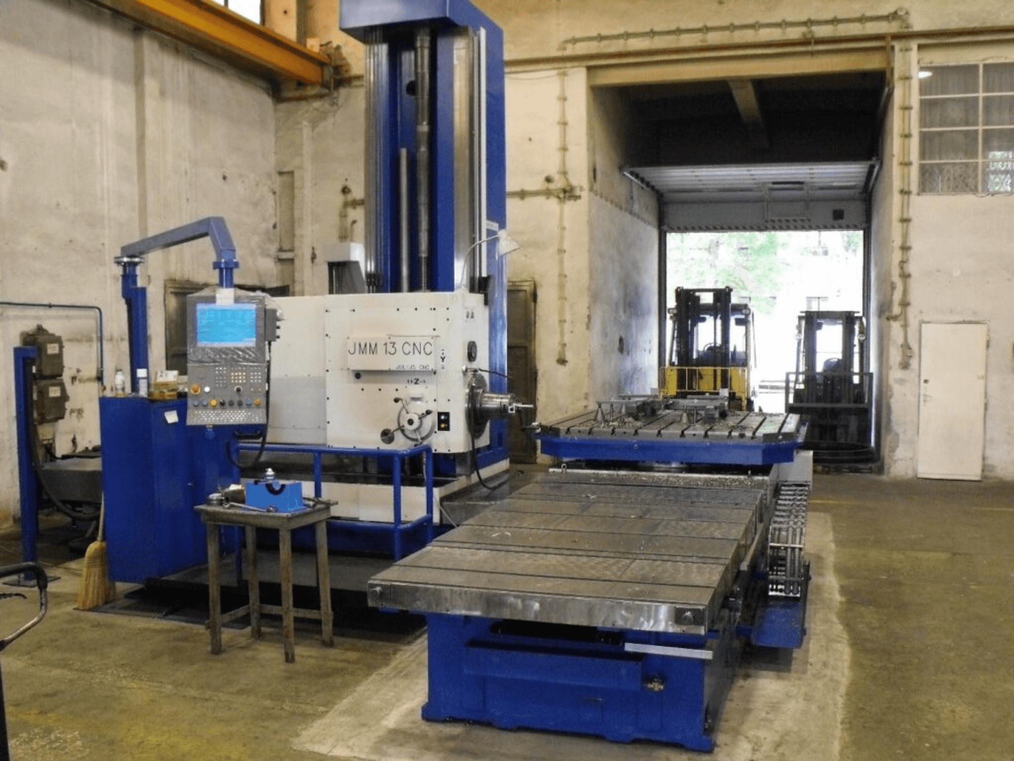 JMM 13 CNC marógép egy műhelyben, elölnézetben, vezérlőpanel, nagy munkaasztal és ipari háttér.
