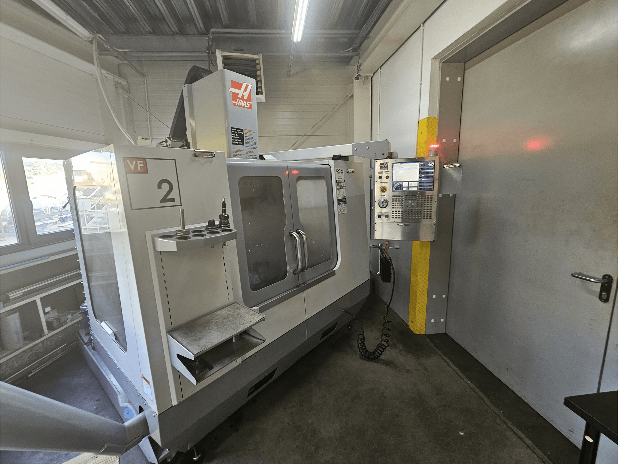 Haas VF-2 CNC marógép, előlnézet, a vezérlőpanel, a szerszámtartók és a munkaterületre nyíló ablak látható.
