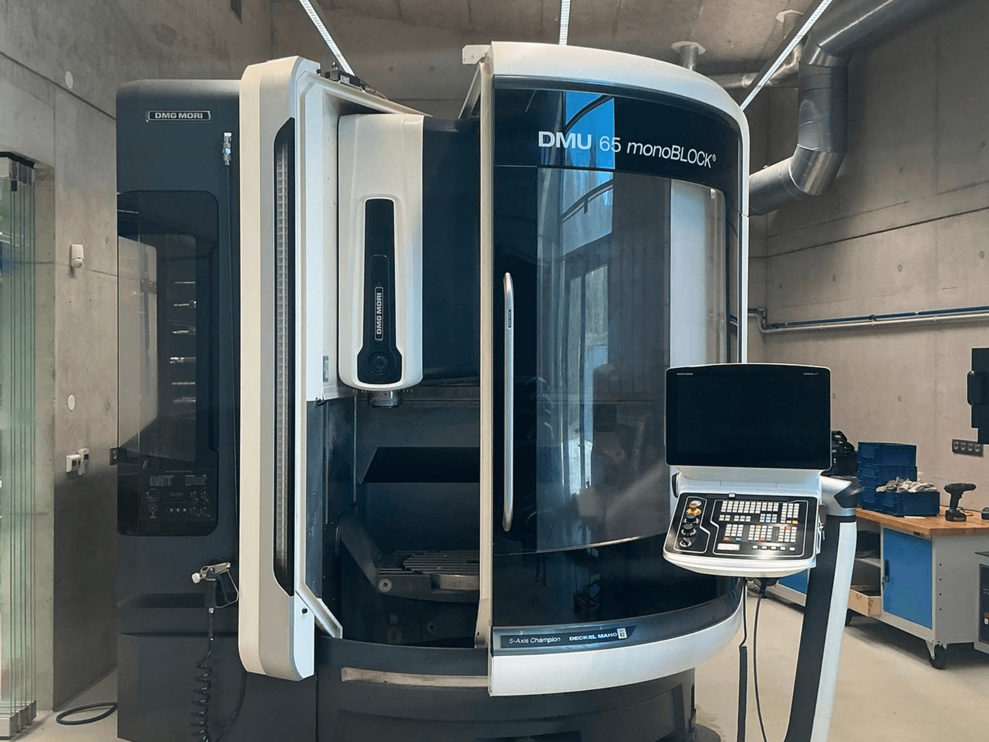 DMG MORI DMU 65 monoBLOCK függőleges megmunkáló központ, elölnézet, amelyen a vezérlőpanel és a gép részletei láthatók műhelyi környezetben.