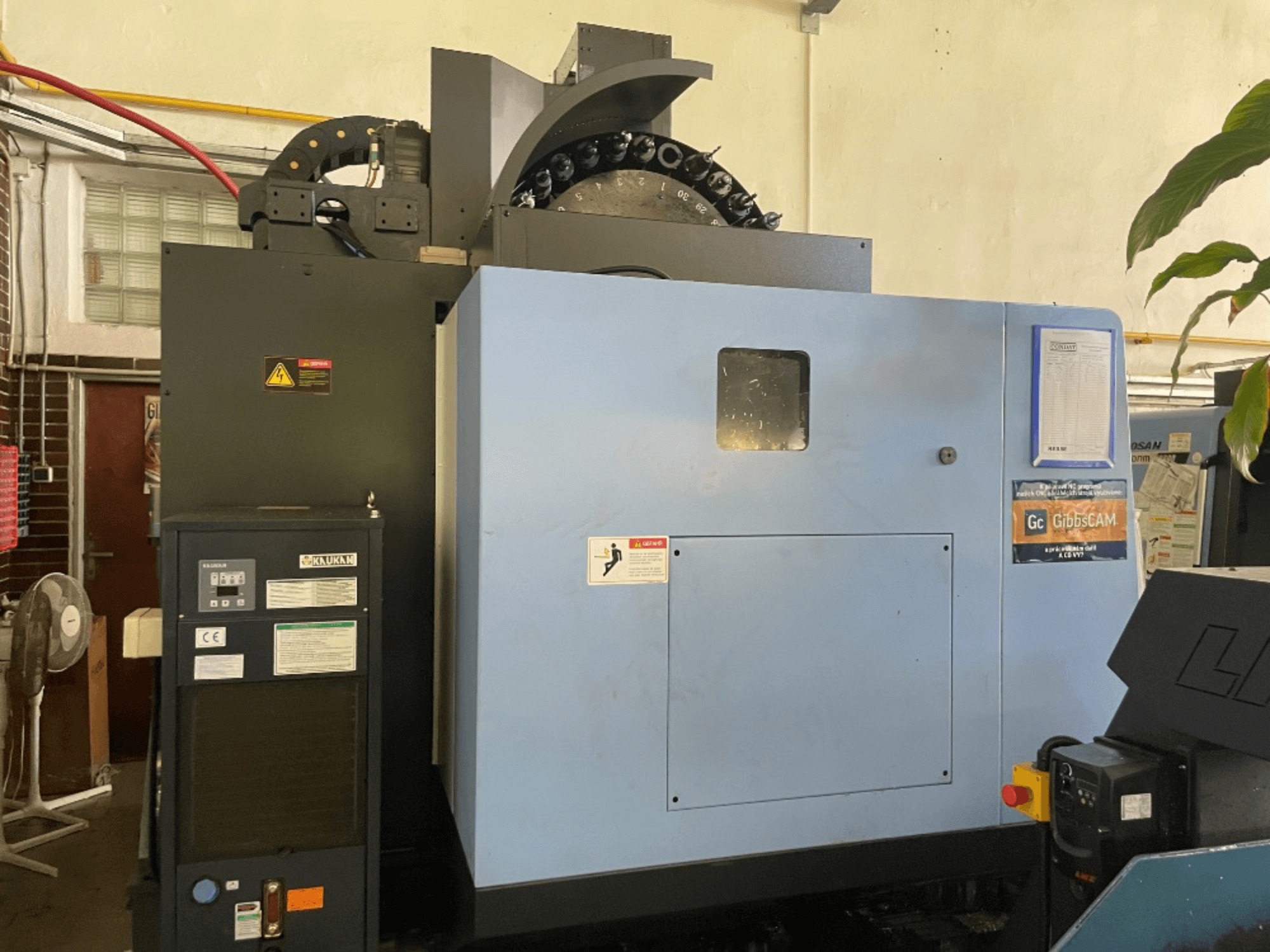 Egy DOOSAN DNM 5700 függőleges megmunkálóközpont előlapja, amelyen a vezérlőpanel, a biztonsági címkék és a gép jellemzői láthatók.