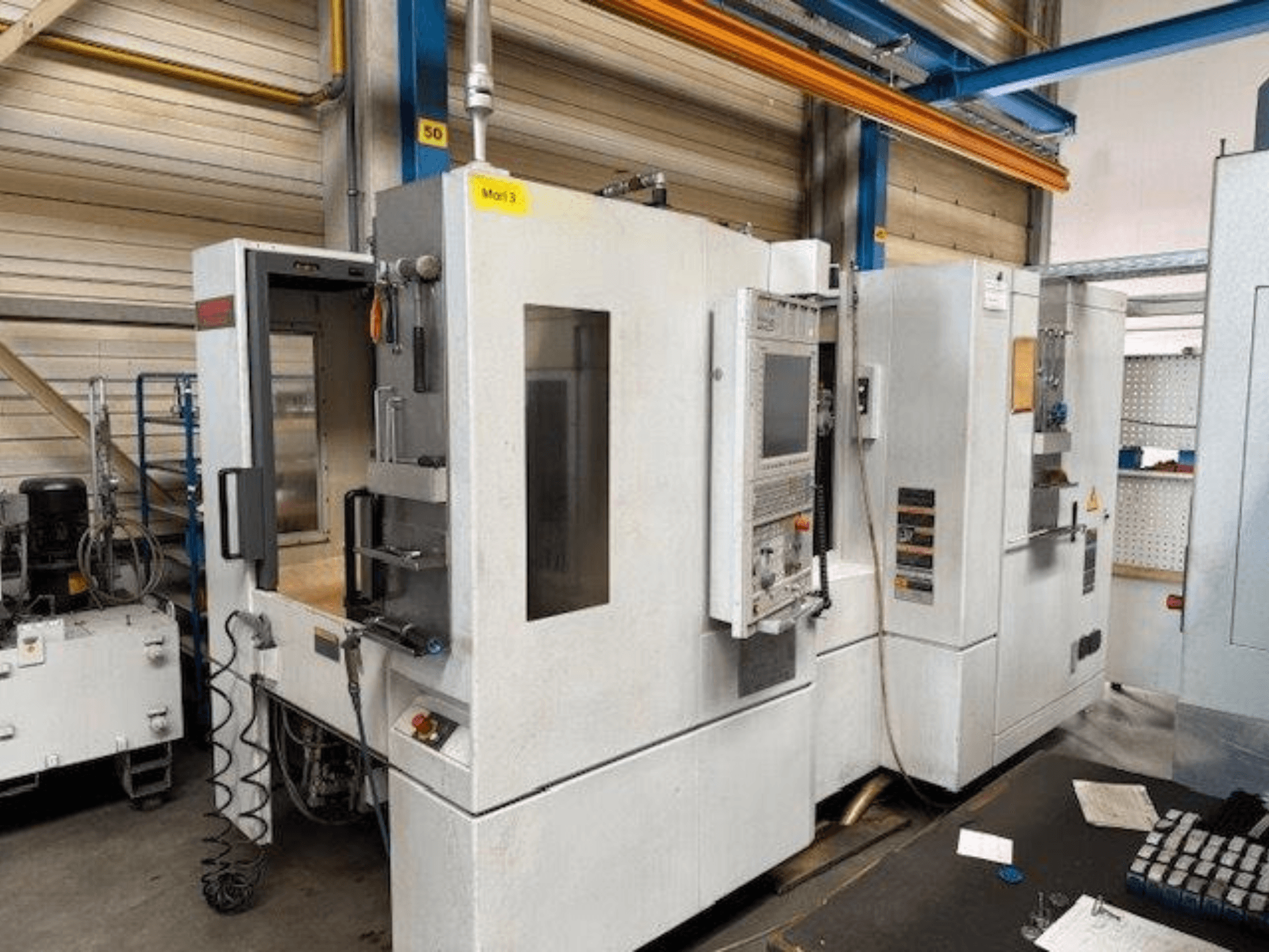 Egy MORI SEIKI NH4000 DCG vízszintes megmunkálóközpont elülső nézete nyitott ajtóval és a kezelőpanel látható, amely a működési teret mutatja.