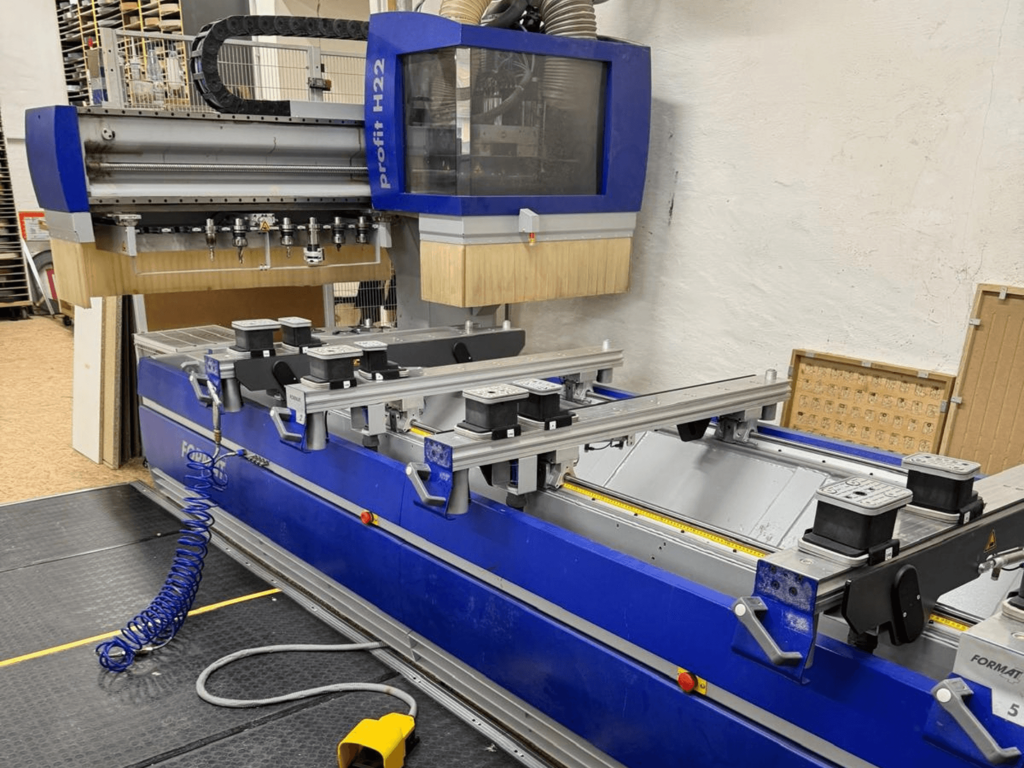 FORMAT4 PROFIT H22 CNC famegmunkáló központ, elölnézet, a kék vázon látható megmunkáló szerszámokkal és rögzítőbilincsekkel.