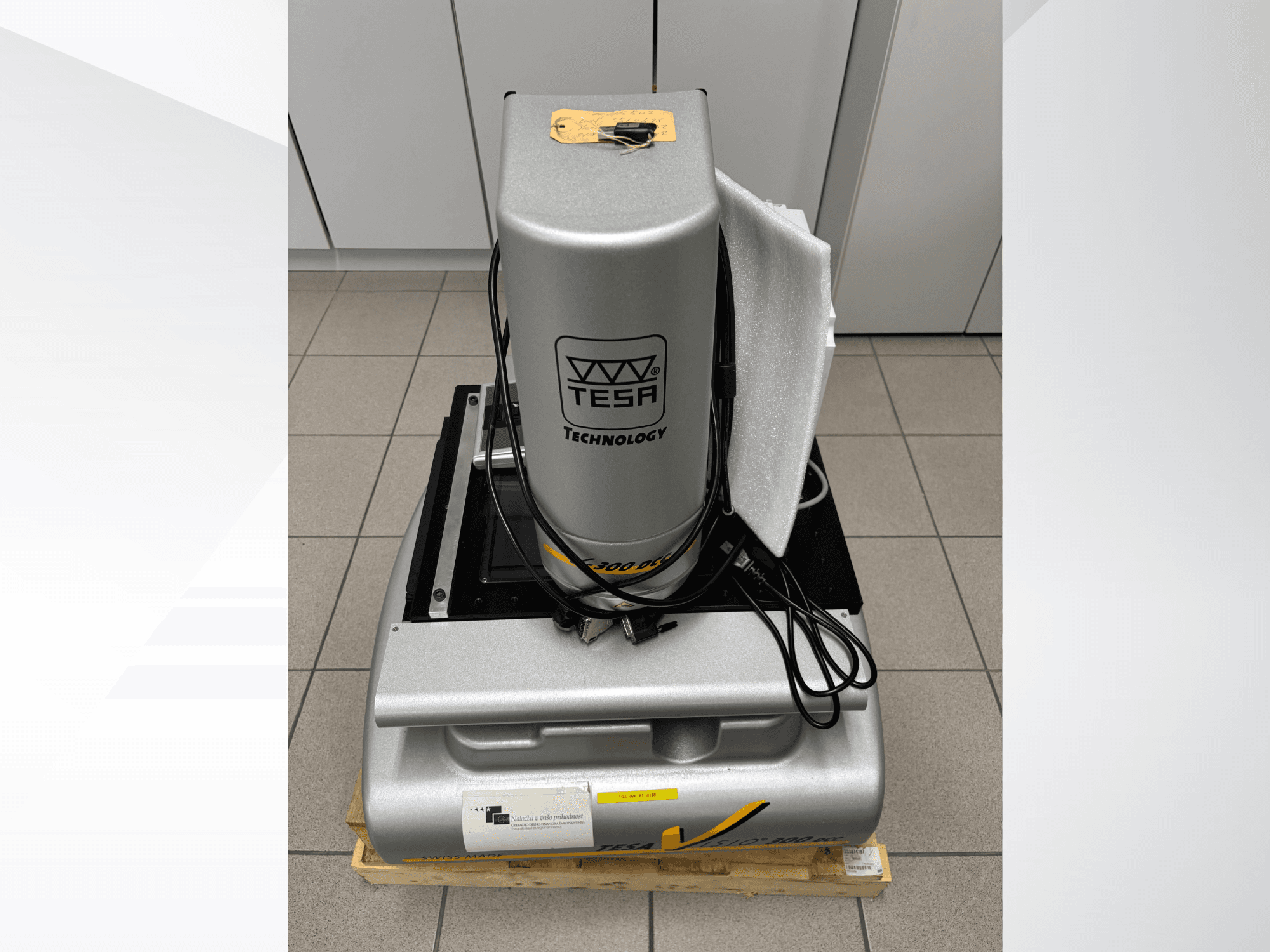 TESA Visio 300 DCC optikai mérőgép elölnézetben, kábelekkel, fa raklapon, védőcsomagolás látható.