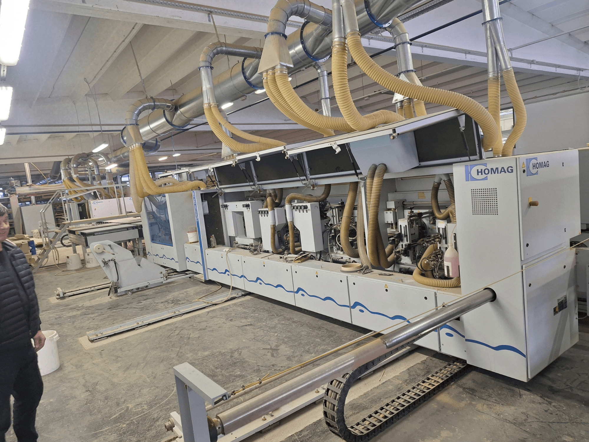 HOMAG famegmunkáló gép gyári környezetben, elölnézetben több orsó és porelszívó rendszer látható.