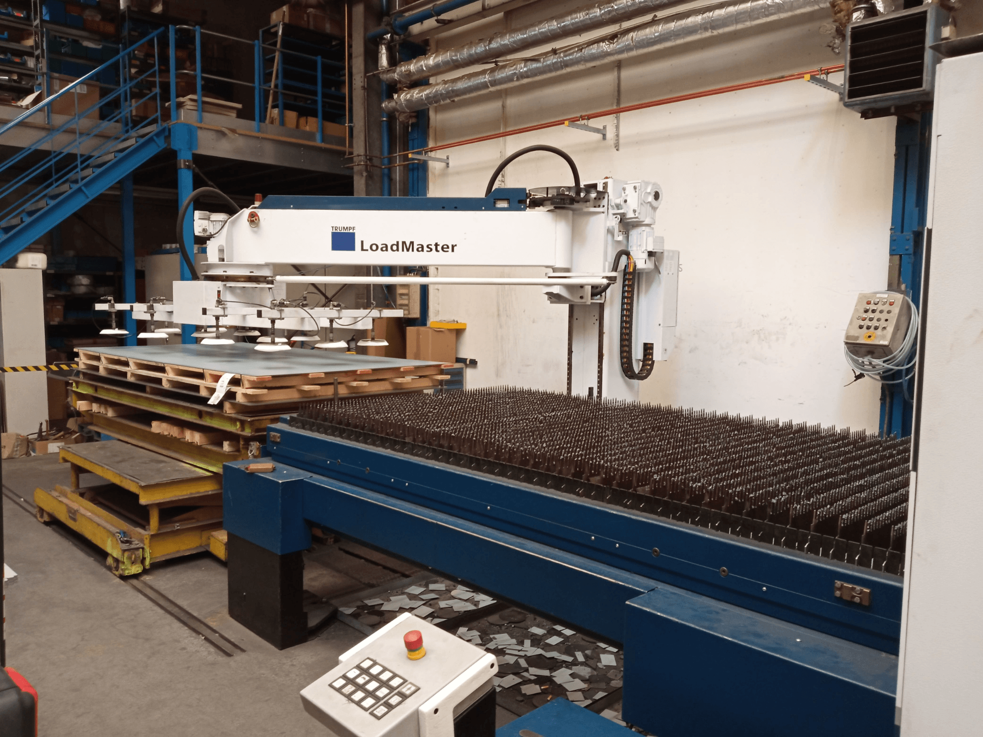 A TRUMPF TruLaser 3030 CO₂-lézervágógép oldalnézetben, LoadMasterrel és anyagpalettákkal.