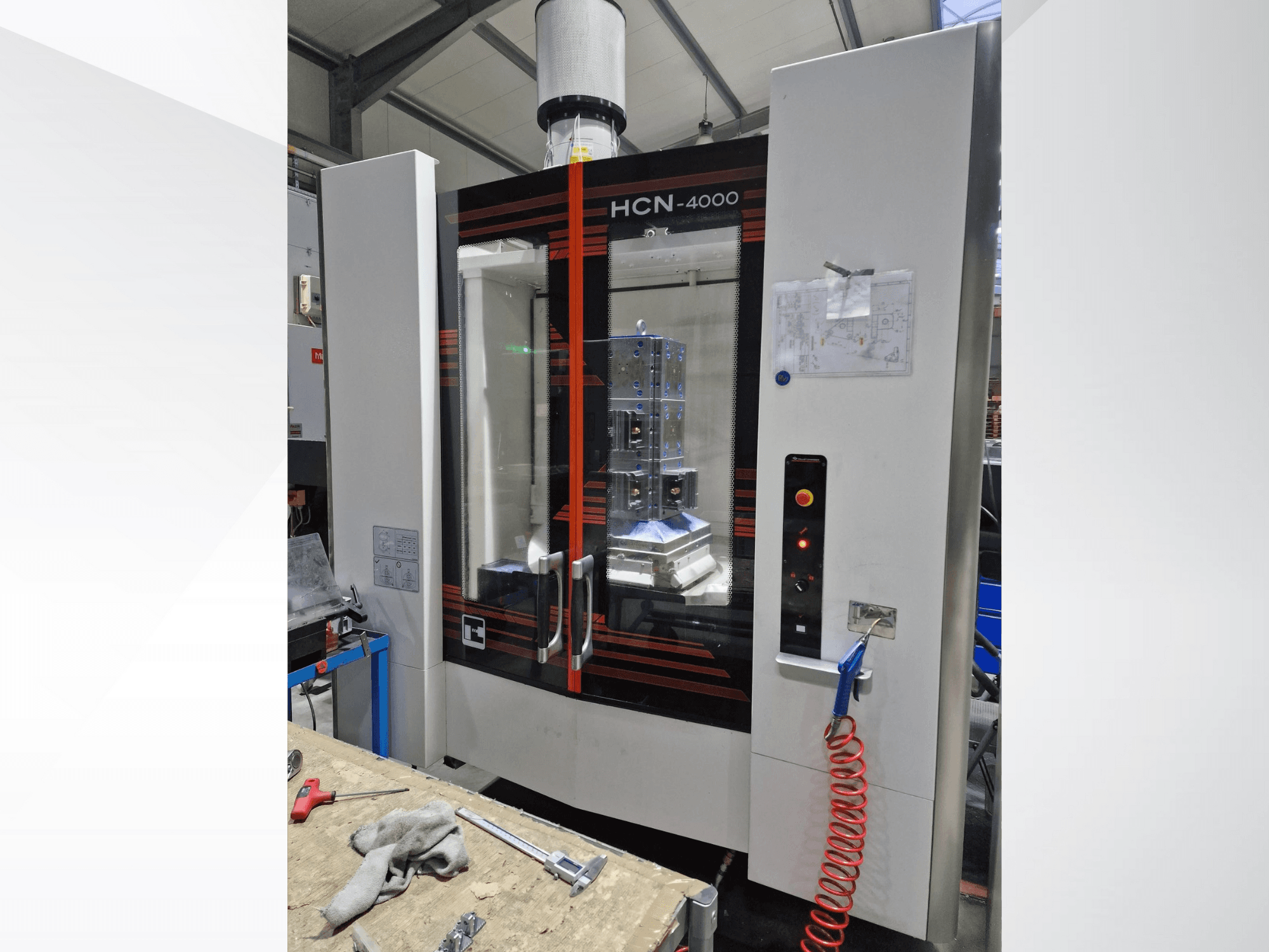 HCN-4000 CNC-gép elölnézetben, üvegpanel, vezérlőpanel gombokkal és egy mellékelt tervrajz.