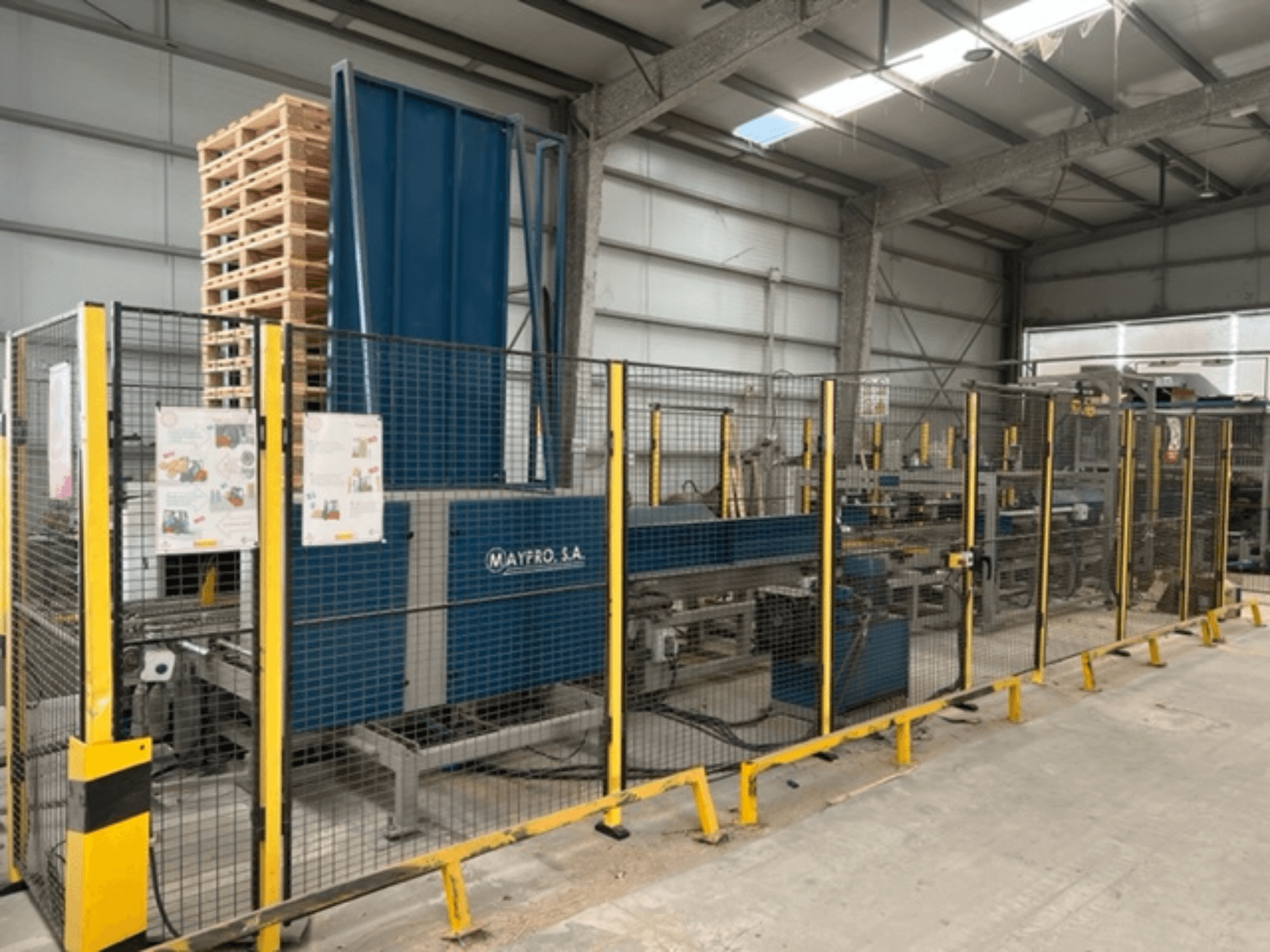 A Maypro S.A. ipari raklapcsomagoló gép egy raktárban, biztonsági hálóval és kezelőszervekkel, oldalnézet.