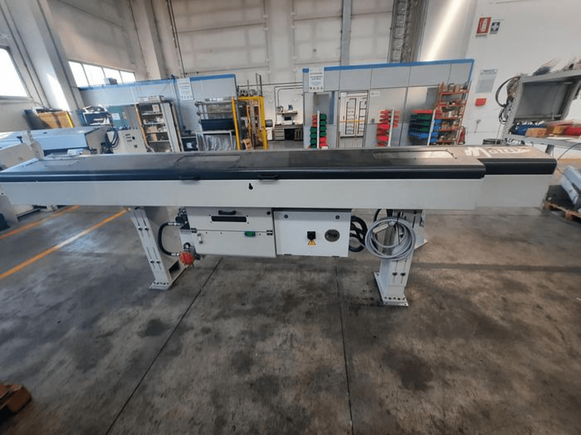 Fém szállítóasztal sima fekete felülettel, oldalnézetben, kezelőgombokkal és kábelekkel; a márka logója részben látható.