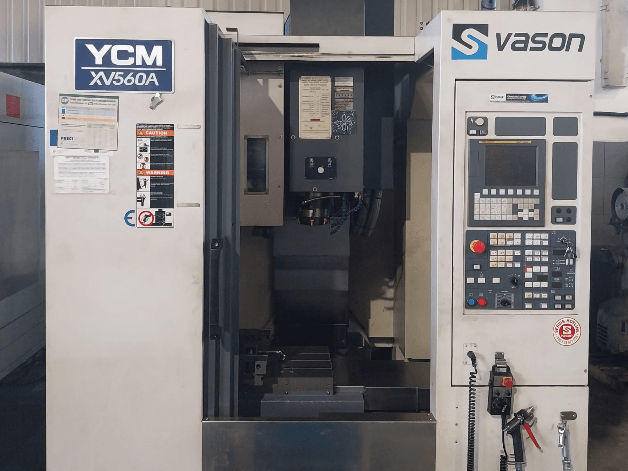 Az YCM XV 560A függőleges megmunkálóközpont előlapja, a vezérlőpanel és a munkaasztal, a megmunkáló alkatrészekkel.