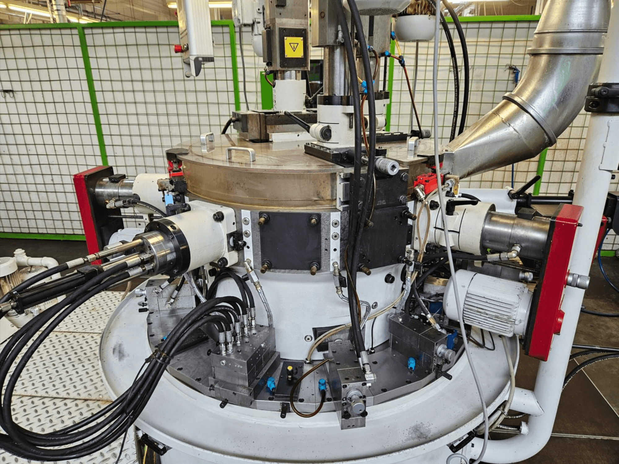 Közelkép egy ipari gépről, hidraulikatömlőkkel, fém alkatrészekkel és forgó alappal. Márka nem látható.