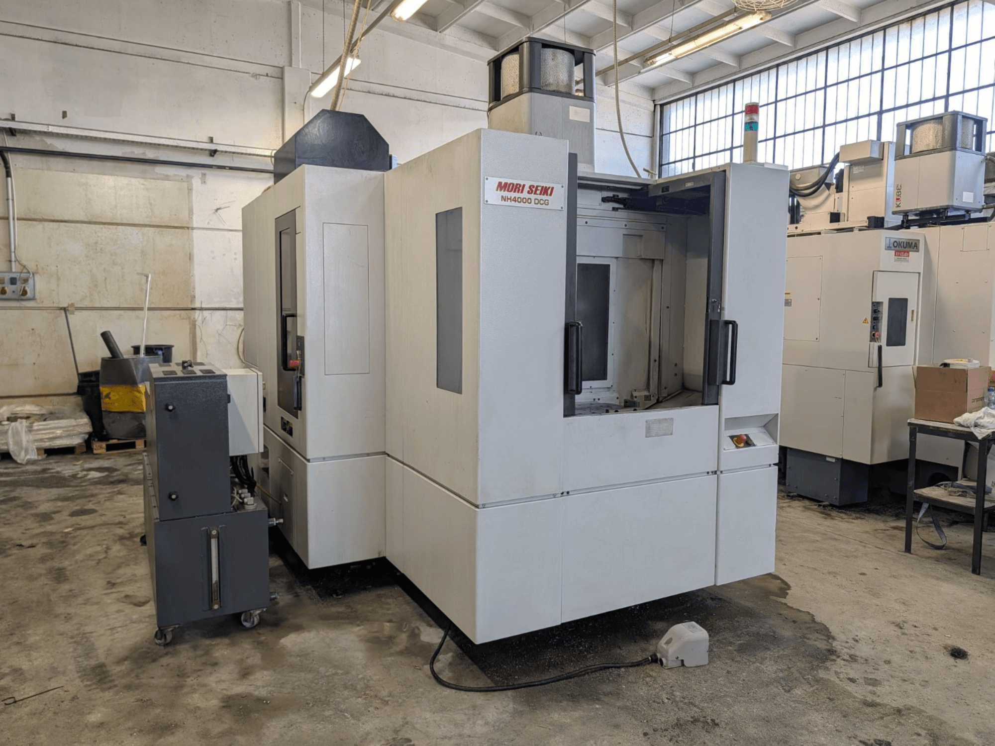MORI SEIKI NH 4000 DCG vízszintes megmunkálóközpont, előlnézet, a vezérlőpanel és a munkaterület bemutatása, szürke és fehér kivitelben.