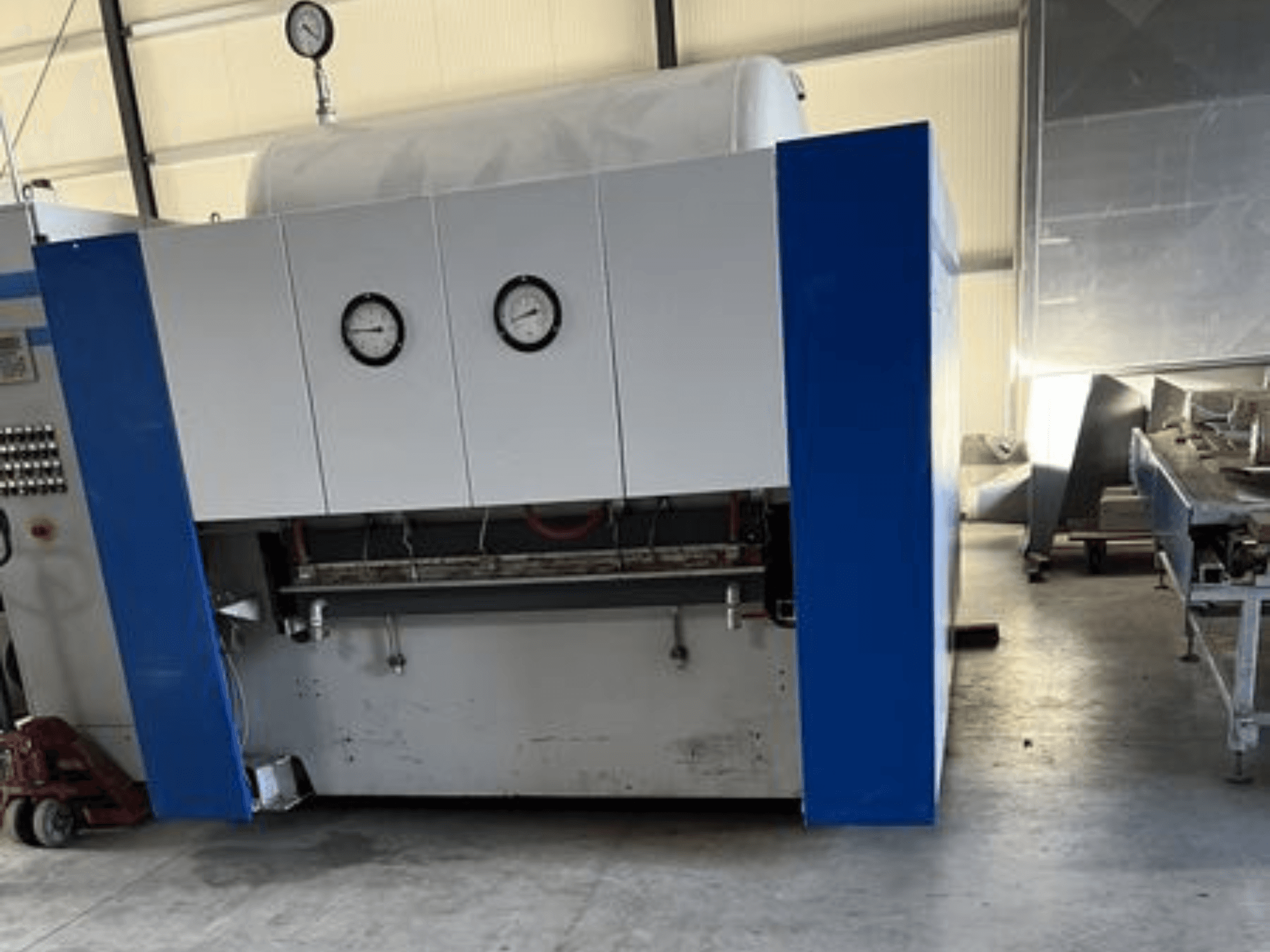 Kék-fehér ipari gép két nyomásmérővel, elölnézetben, vezérlőpanellel és a szomszédos berendezésekkel.