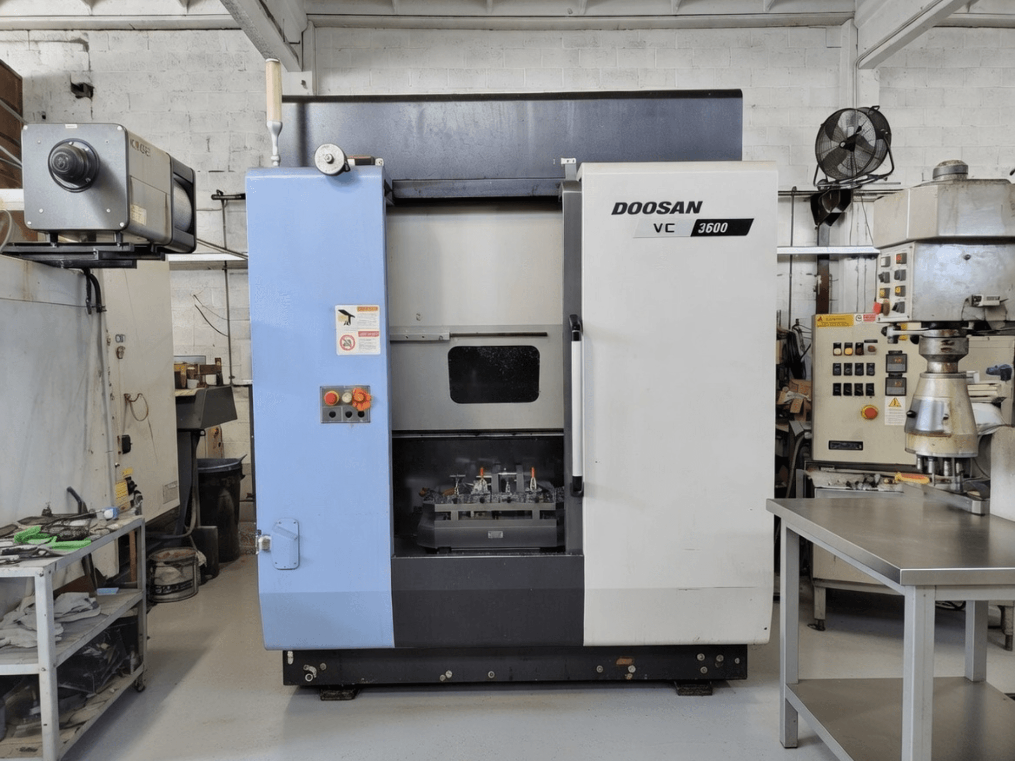 DOOSAN VC 3600 függőleges megmunkálóközpont elölnézetben, a vezérlőpanellel és a nyitott ajtóval, amely feltárja a munkaterületet.