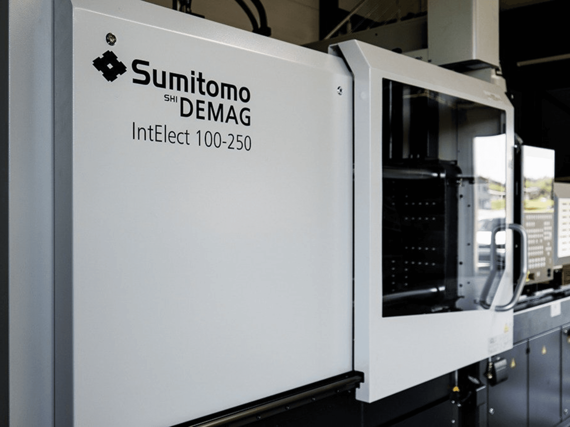 A SUMITOMO SHI DEMAG IntElect 100/250 elektromos fröccsöntőgép elölnézete, a vezérlőpanellel és a biztonsági berendezésekkel együtt.