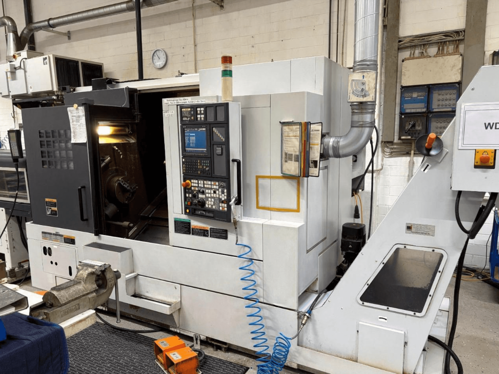MORI SEIKI NL 2500 SY esztergapad-központ, előlnézet, a vezérlőpanel és a megmunkálási terület. Látható hűtőfolyadék-rendszer és tartozékok.