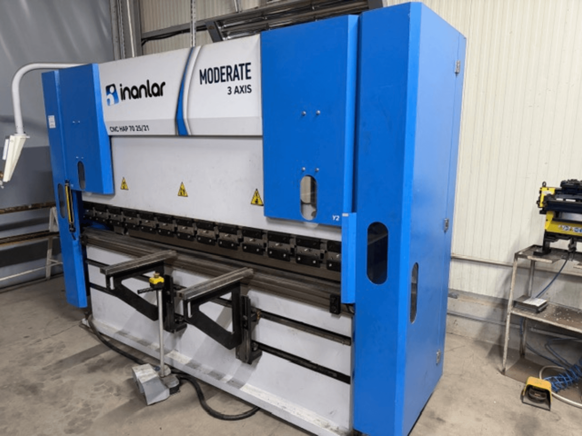 Inanlar Moderate 3 tengelyes CNC-gép kék színben, elölnézetben, a karosszérián látható vezérlőkarokkal és biztonsági címkékkel.