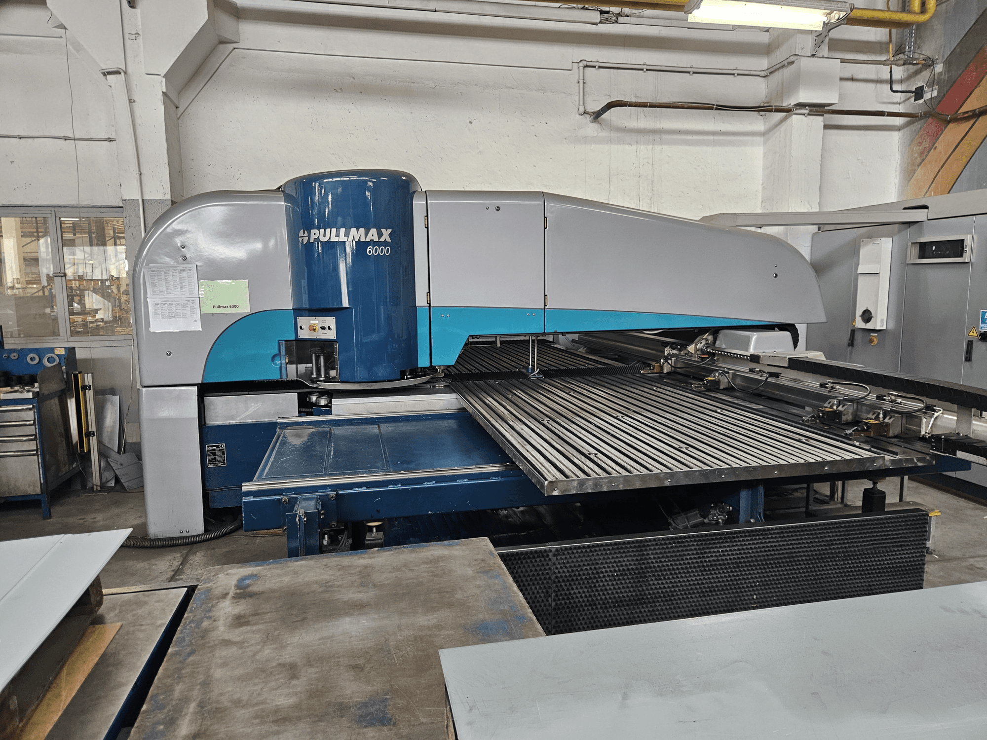 A Pullmax 6000 CNC lyukasztógép elülső nézete, amely a nagyméretű síkágyat és a fémkeretet mutatja be műhelykörnyezetben.