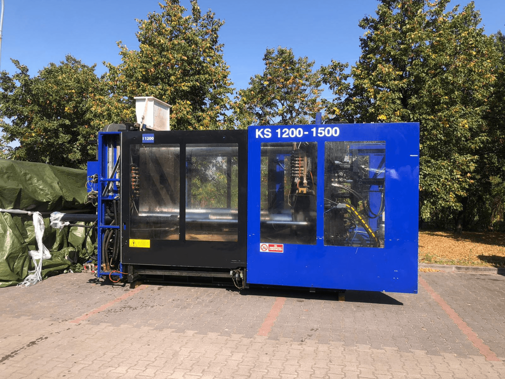 Hidraulikus fröccsöntőgép ITALTECH KS 1200 8300 ES, oldalnézet, a kezelőszervek és a gép részleteinek bemutatása parkos környezetben.