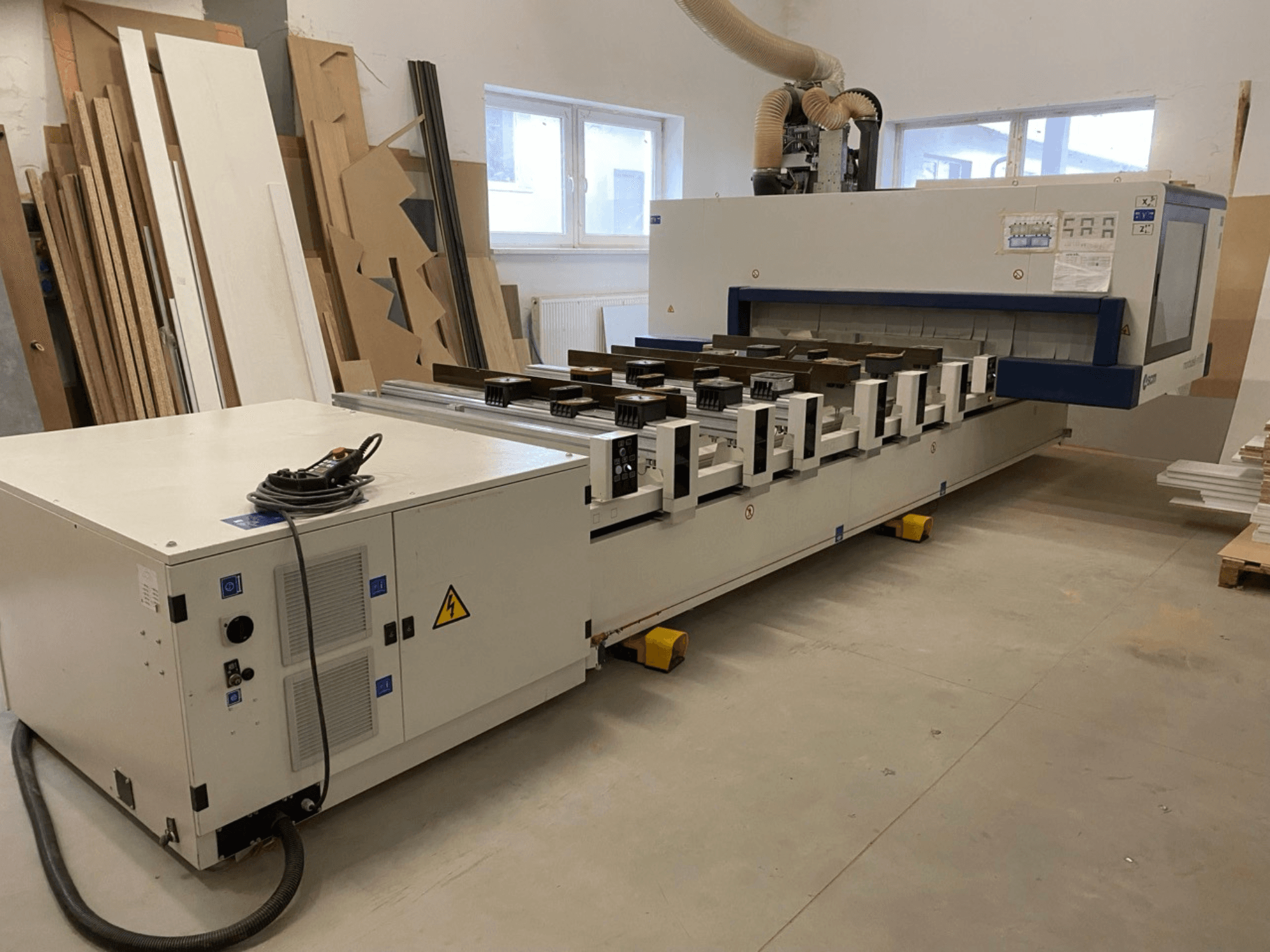 Az SCM Morbidelli gyártmányú M100 CNC faipari megmunkáló központ egy műhelyben, elölnézetből, a vezérlőpanellel és a porelszívóval együtt.