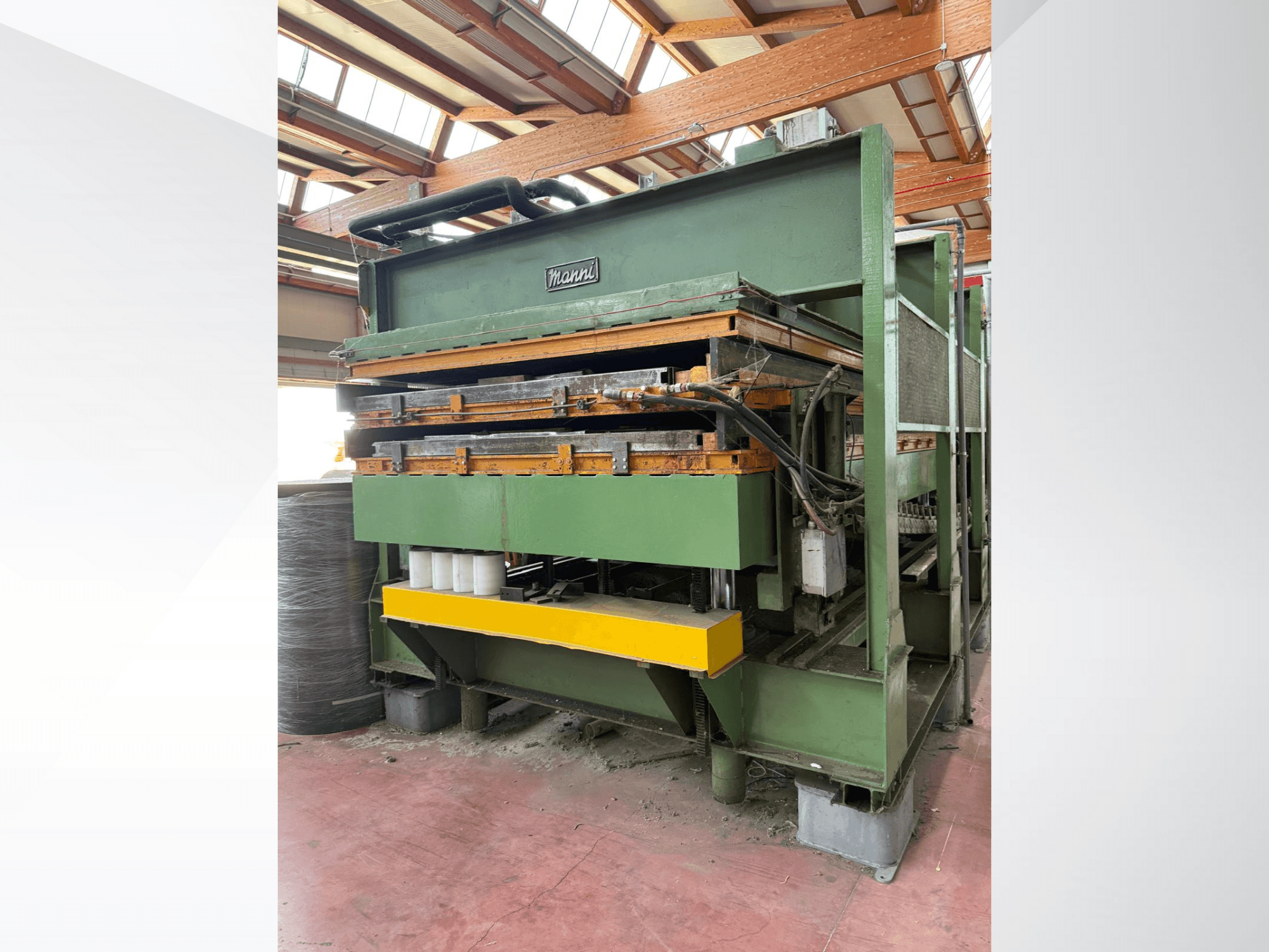 Manni hidraulikus prés, oldalnézet, zöld fémtest, sárga alap és több hidraulikavezeték látható.