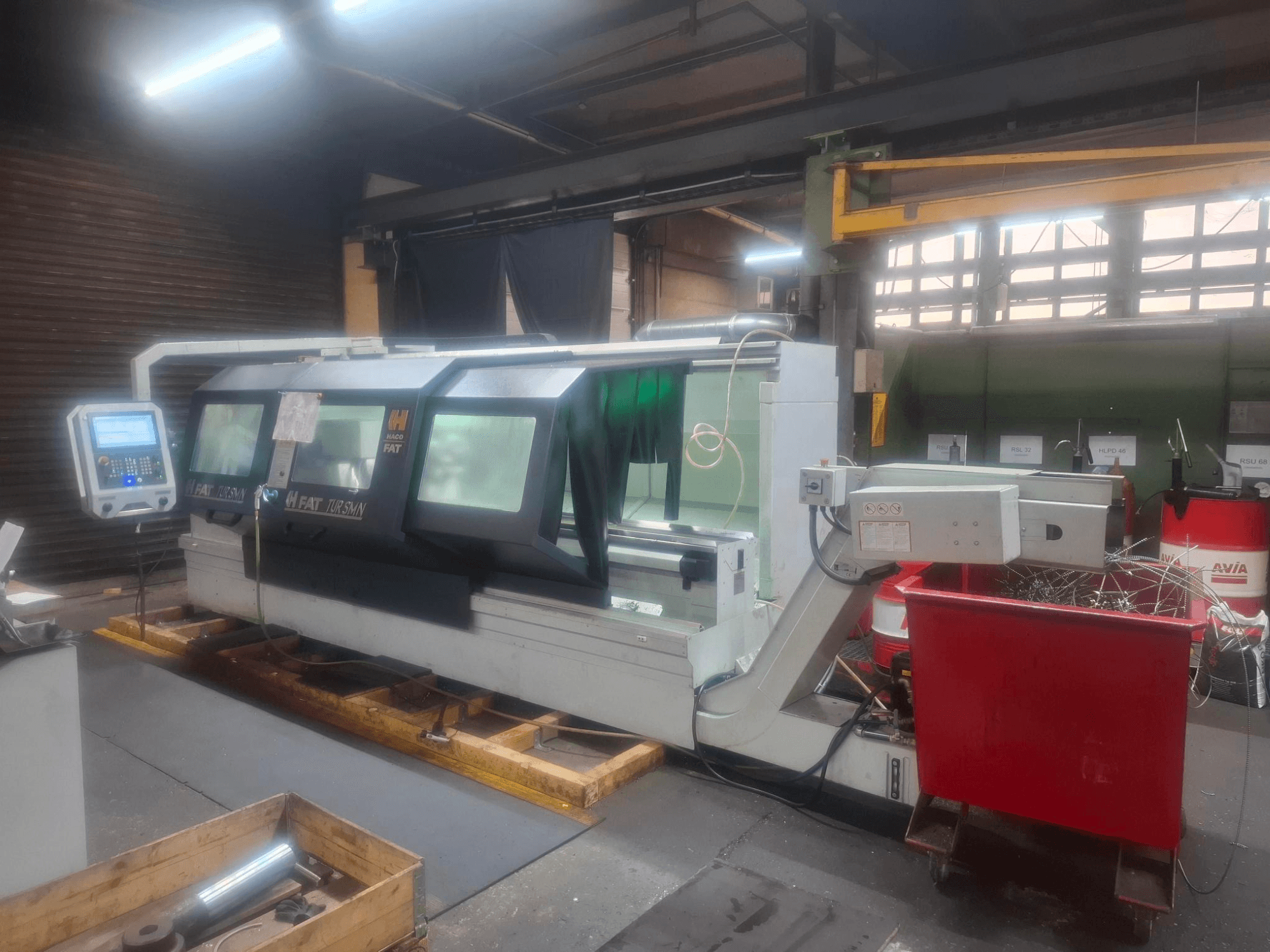 Egy FAT Tursan CNC-gép előlnézetből, vezérlőpanellel, fából készült raklapokon elhelyezve egy műhelyben.