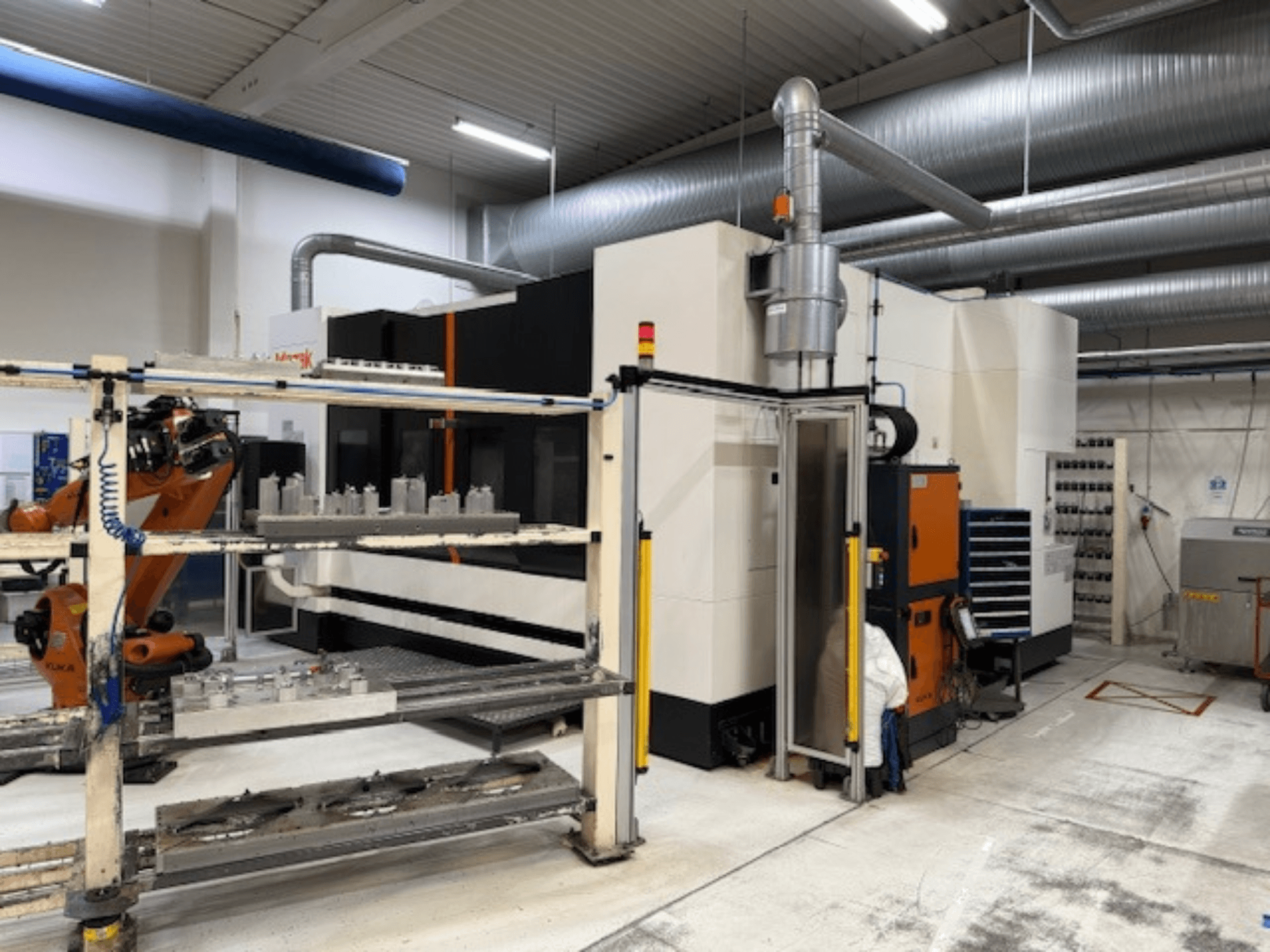Ipari CNC-gép robotkarral és biztonsági korlátokkal, a berendezés elülső nézete egy szellős munkaterületen.