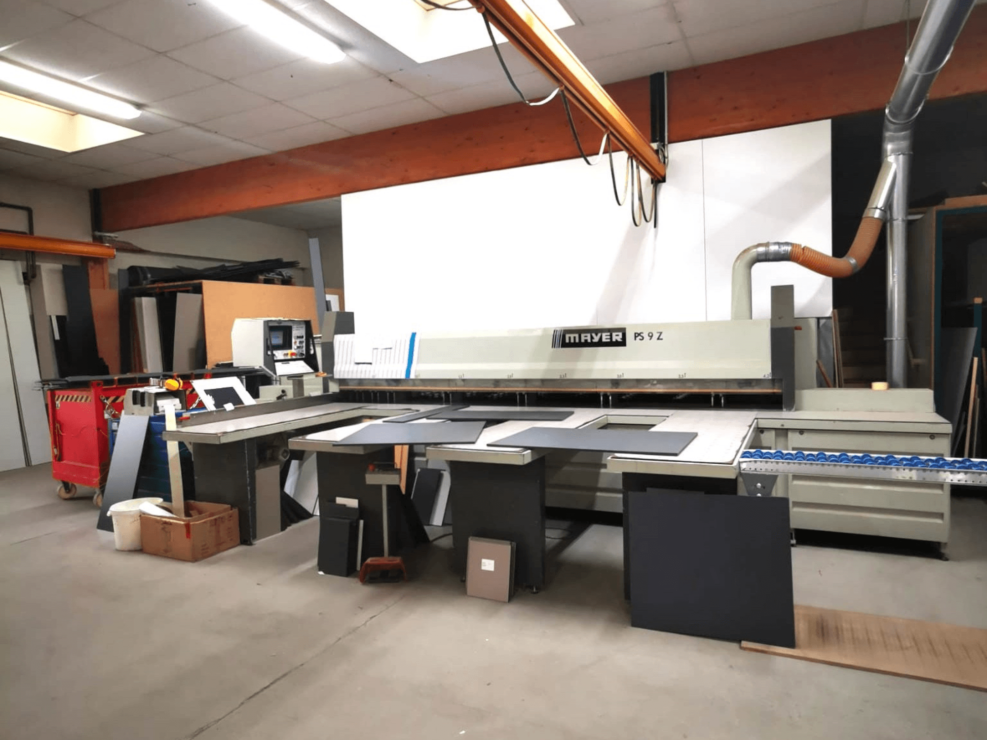 MAYER PS9 Z vágógép egy műhelyben, elölnézetben, láthatóak a különböző anyagok és a szállítószalagrendszer.