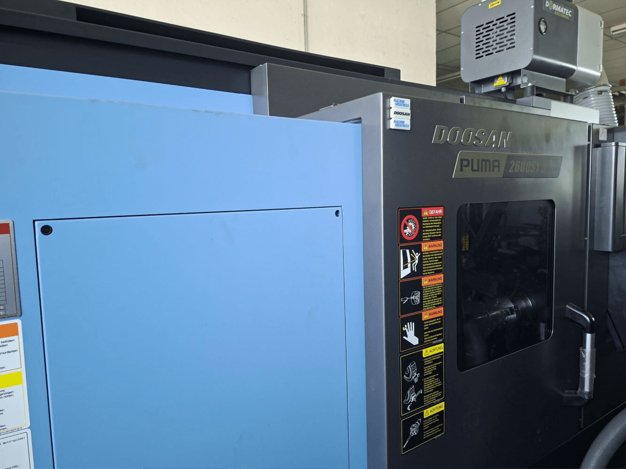 DOOSAN PUMA 2600 SY II vízszintes esztergagép, előlnézet, biztonsági címkék és kék burkolat.