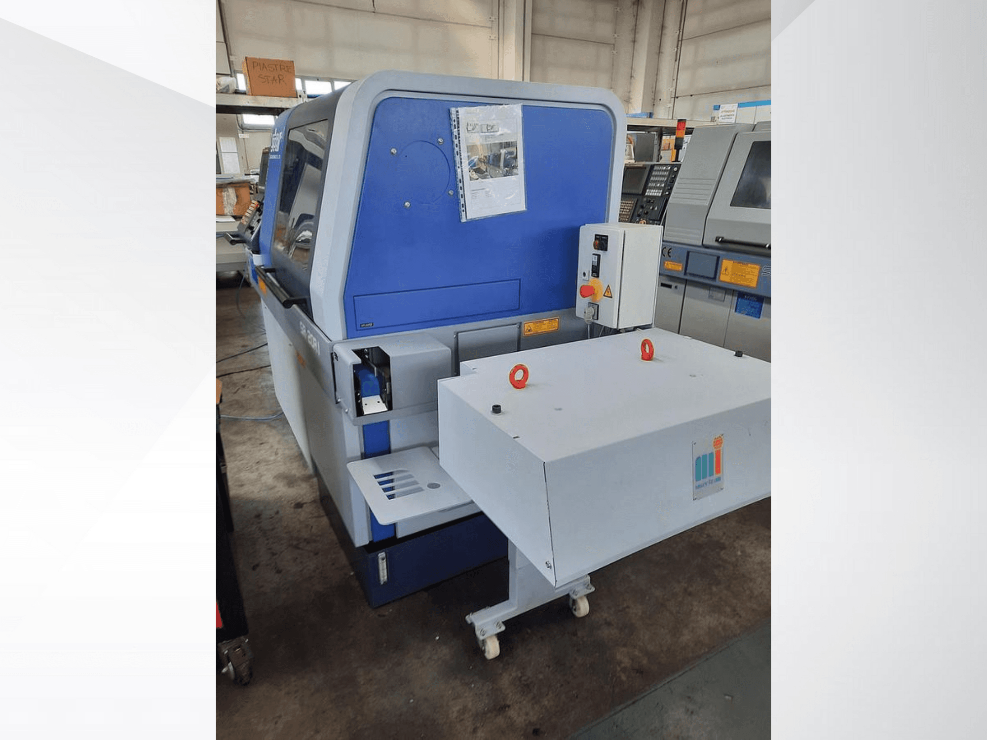 Kék ipari gép fehér szállítószalaggal, a vezérlőpanel és a csatlakoztatott biztonsági berendezések láthatóak, oldalnézetben.