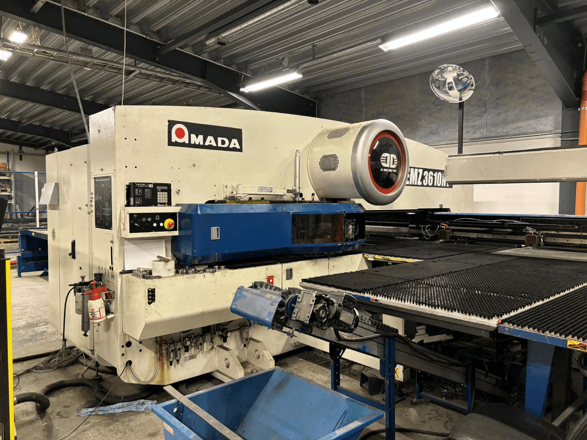 Amada EMZ3610H lyukasztóprés elölről nézve; a kezelőszervek, a kék ágy és a biztonsági berendezések jellemzői.