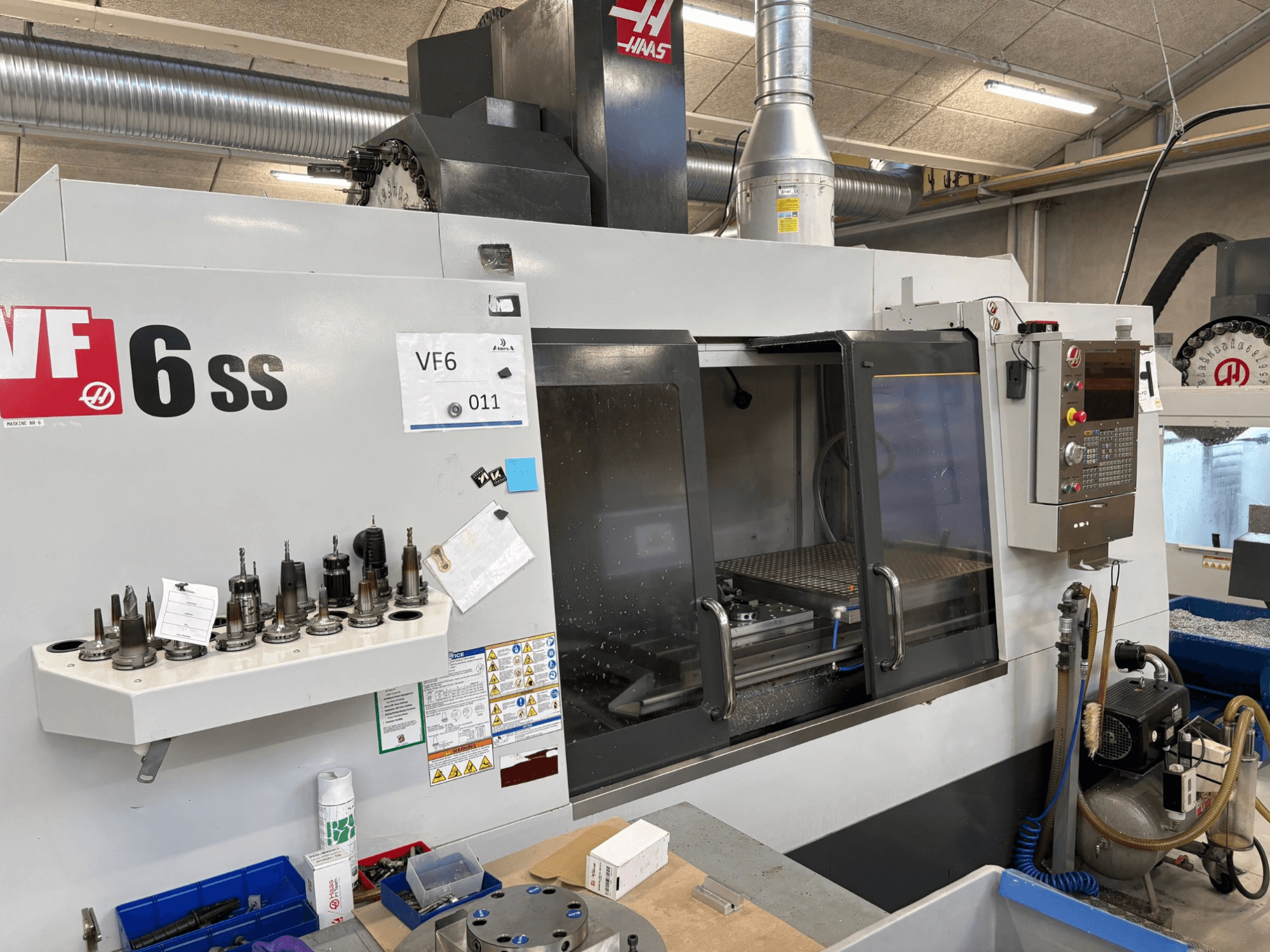Haas VF-6 SS CNC marógép, előlnézet. Különböző szerszámokkal, vezérlőpanellel és látható belső munkaterülettel.
