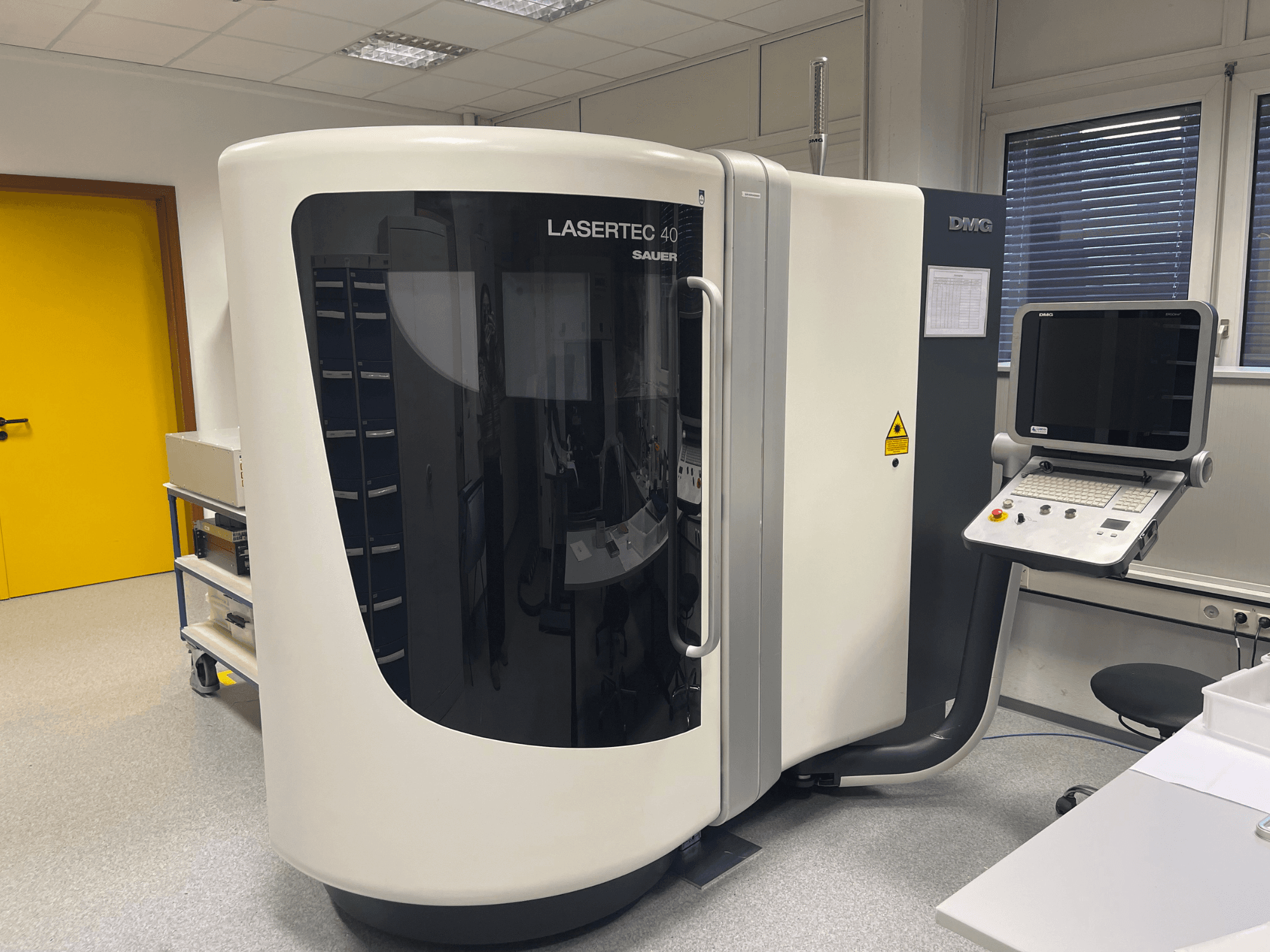 A DMG MORI fehér LASERTEC 40 marógép elölnézetben, kezelőpanel és ergonomikus kialakítás egy jól megvilágított helyiségben.