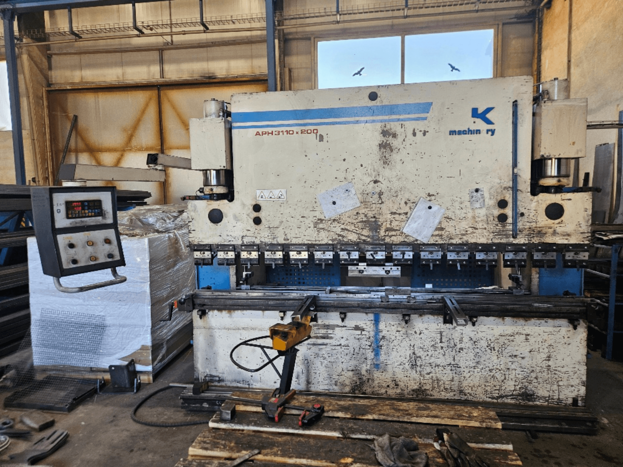 Baykal APH 3110x200 sajtolófék egy műhelyben, elölnézetben, a vezérlőpanel, a fémlemezek és a szerszámok láthatóak.