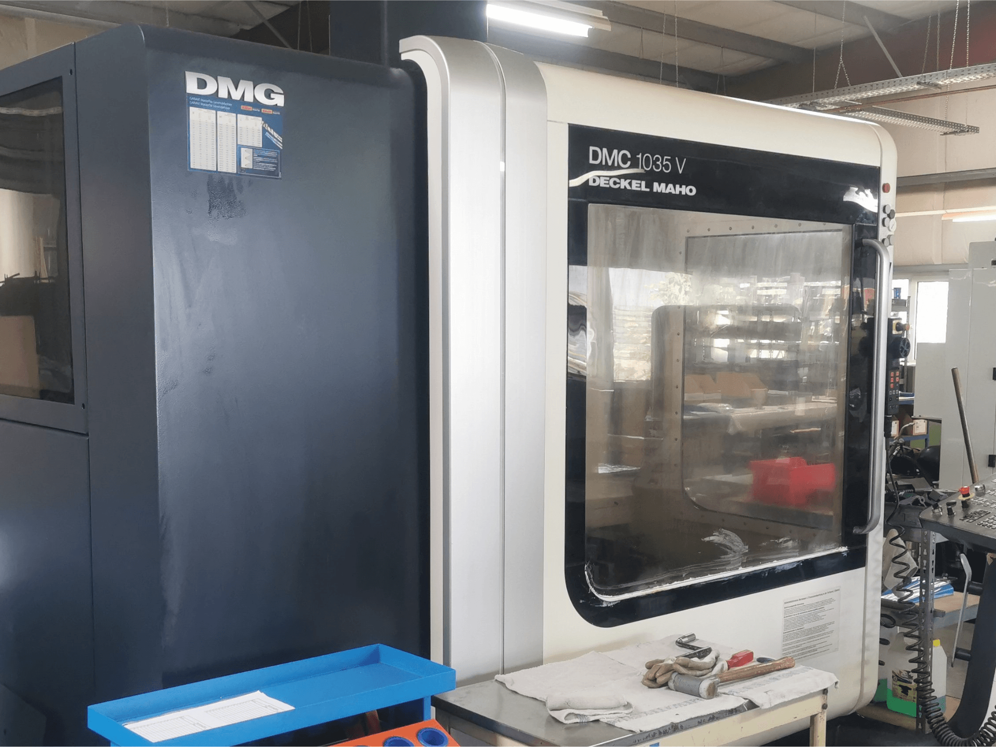DMG DMC 1035 V marógép egy műhelyben, elölnézetben, kék szerszámtálcával és kesztyűvel a felületen.