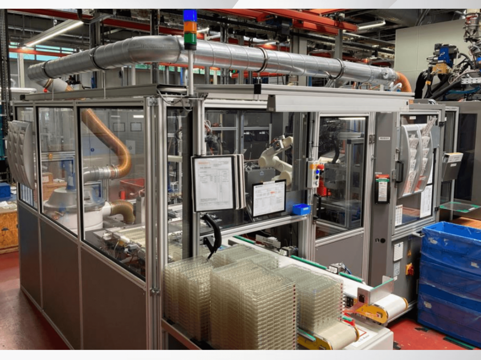 Automatizált összeszerelőgép robotkarral, átlátszó oldallapokkal és egymásra helyezett, átlátszó tárgyakat tartalmazó tartályokkal, elölnézetből.