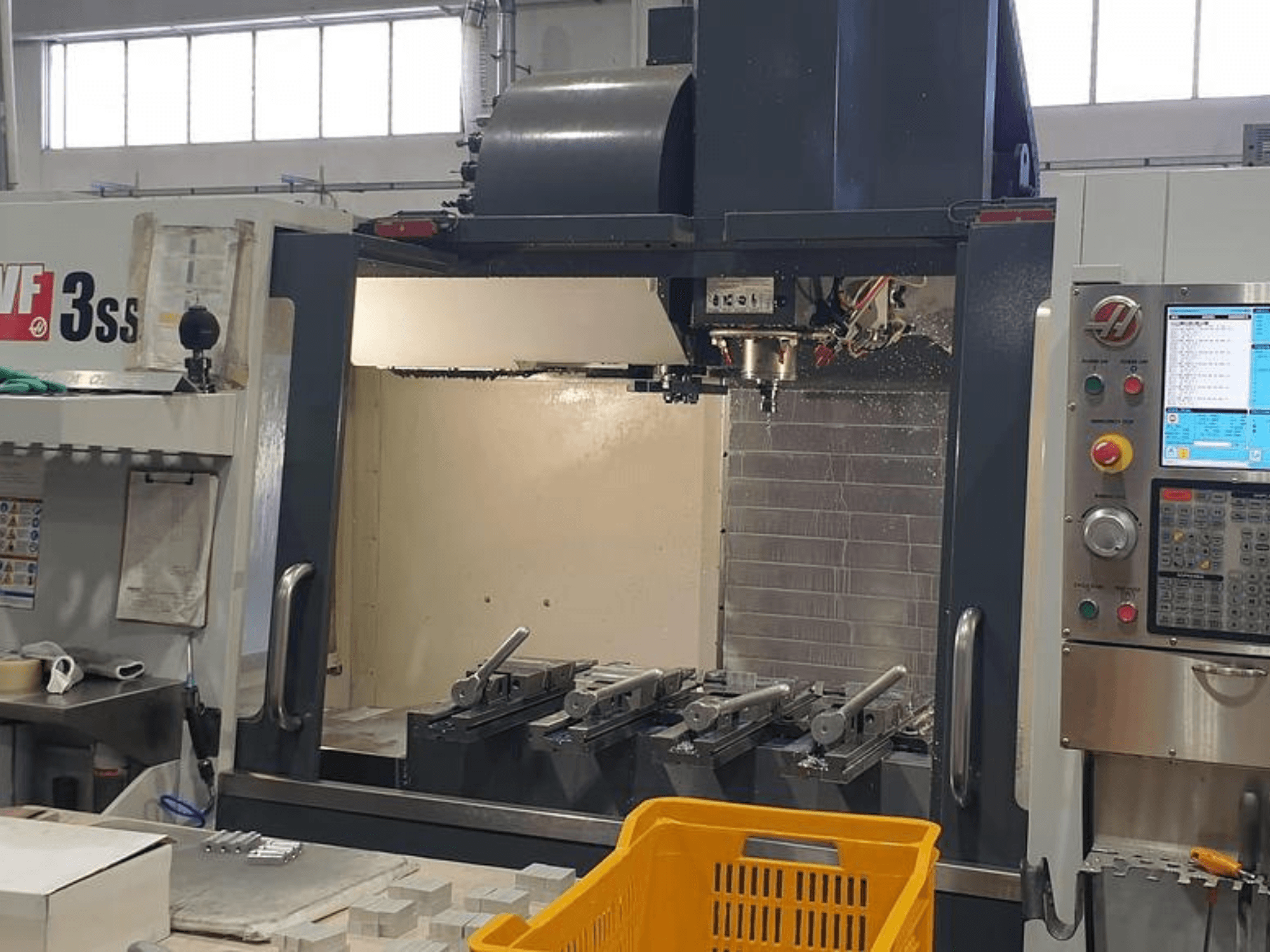 HAAS VF-3SS függőleges megmunkálóközpont, előlnézet CNC vezérlőpanellel, szerszámokkal és narancssárga kosárral.