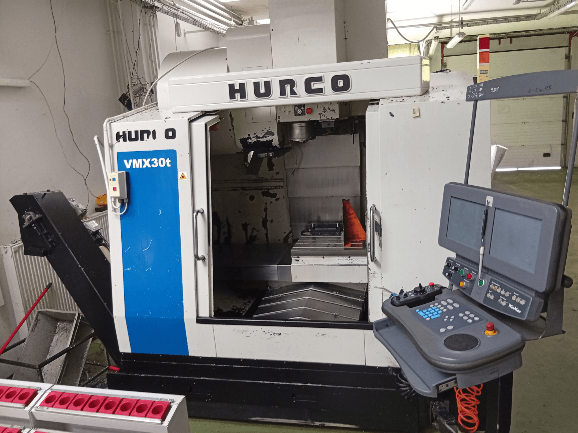 Hurco VMX 30T függőleges megmunkáló központ, elölnézet, a vezérlőpanellel és az orsóterülettel, a munkasztal látható.