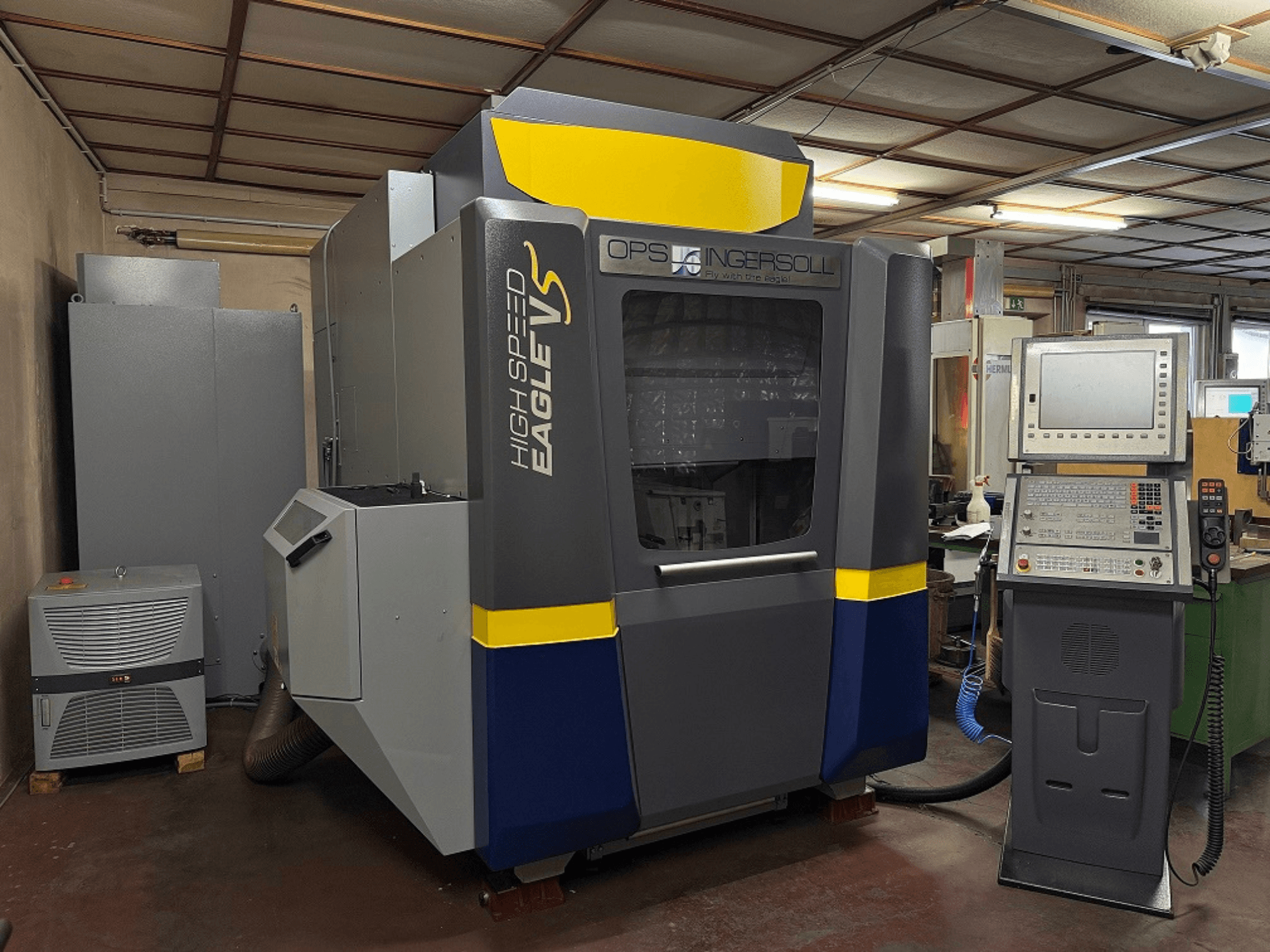 Az OPS Ingersoll nagysebességű Eagle V gépe, oldalnézet, vezérlőpanel és a szomszédos berendezések ipari környezetben.
