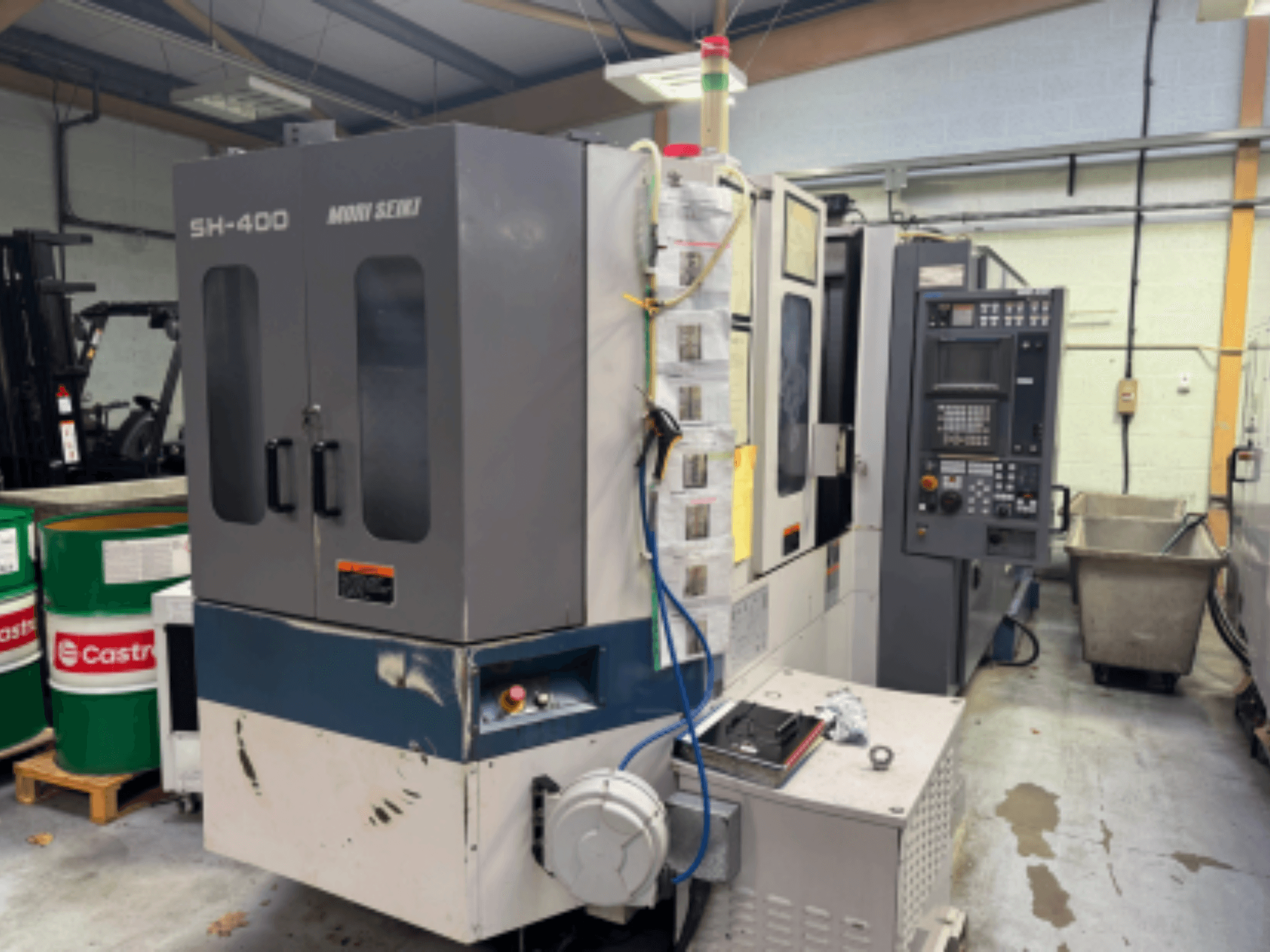 Moni Seiki SH-400 CNC-gép, oldalnézet a vezérlőpanel, az ajtók és a környező ipari környezetről.