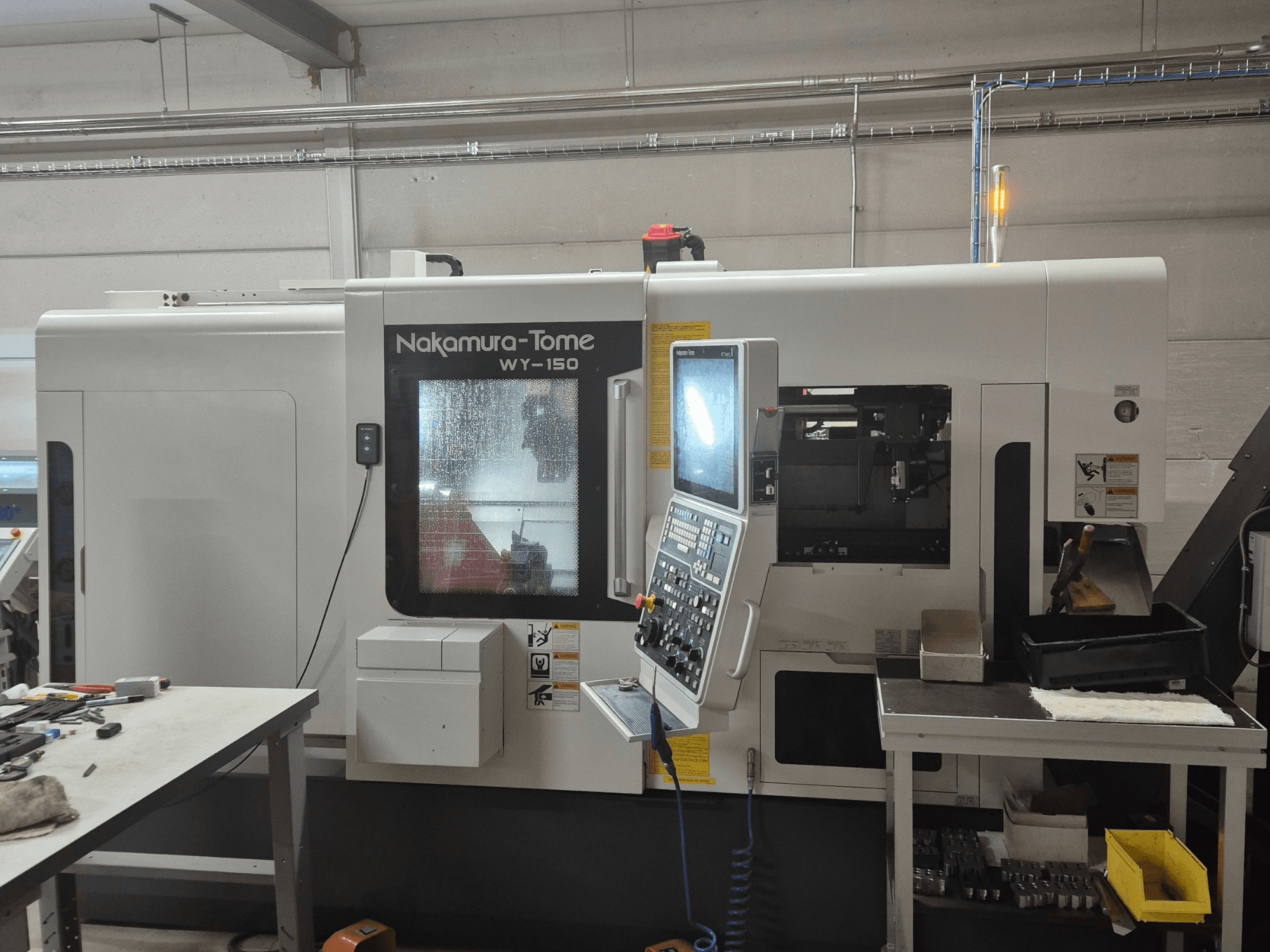Nakamura-Tome WY-150 CNC eszterga oldalnézetben, vezérlőpanellel, átlátszó ablakkal és látható munkaterülettel.