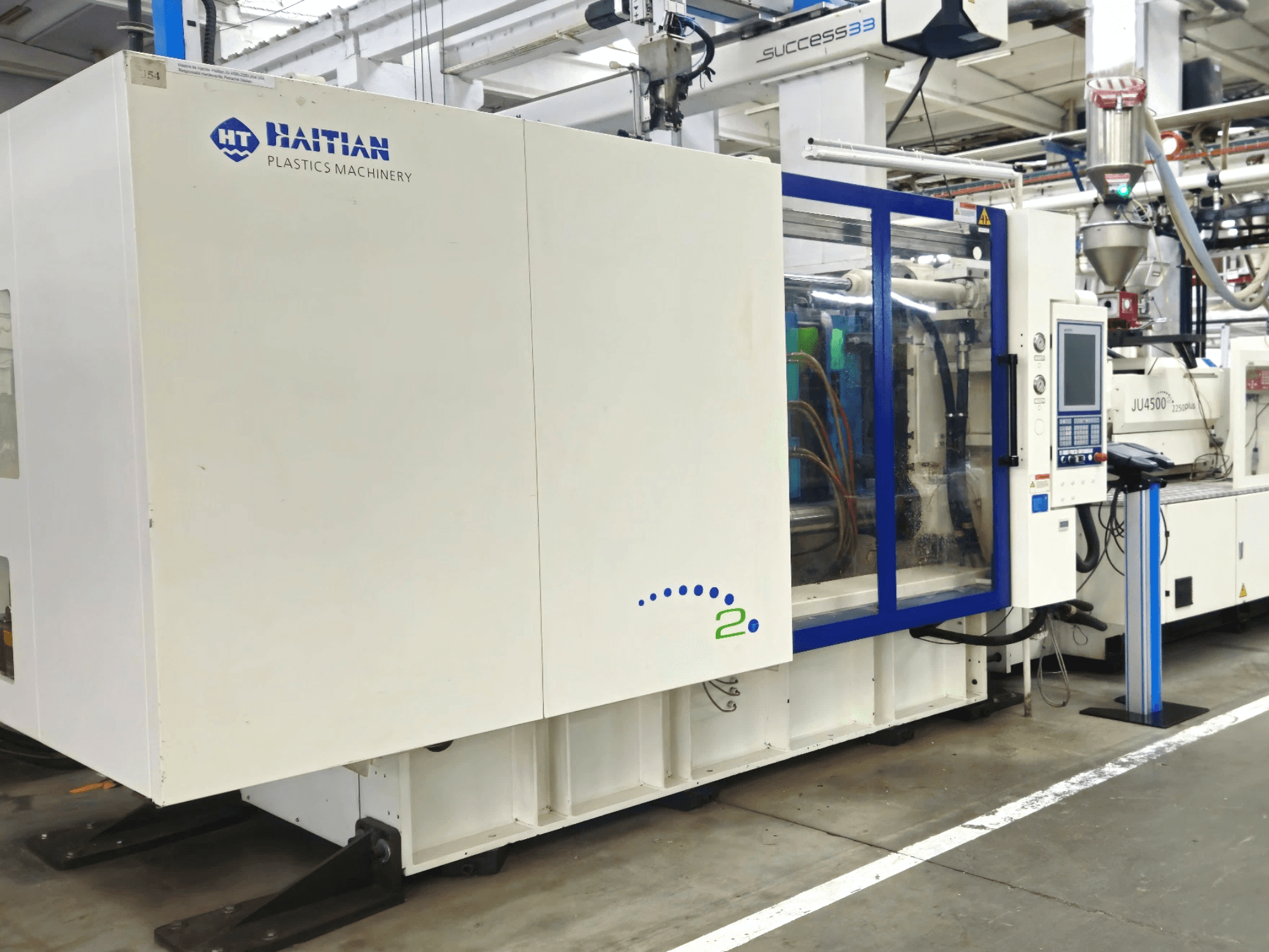 Haiti műanyagipari gépek modellje, elölnézetben, a gépet bemutató vezérlőpanel és látható csövek, ipari környezetben.